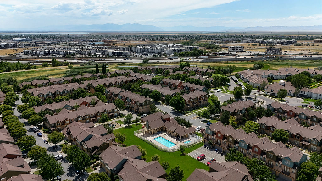 Aerial perspective showcasing a residential community with multi-story townhomes, a central swimming pool with surrounding patio, and mature landscaping