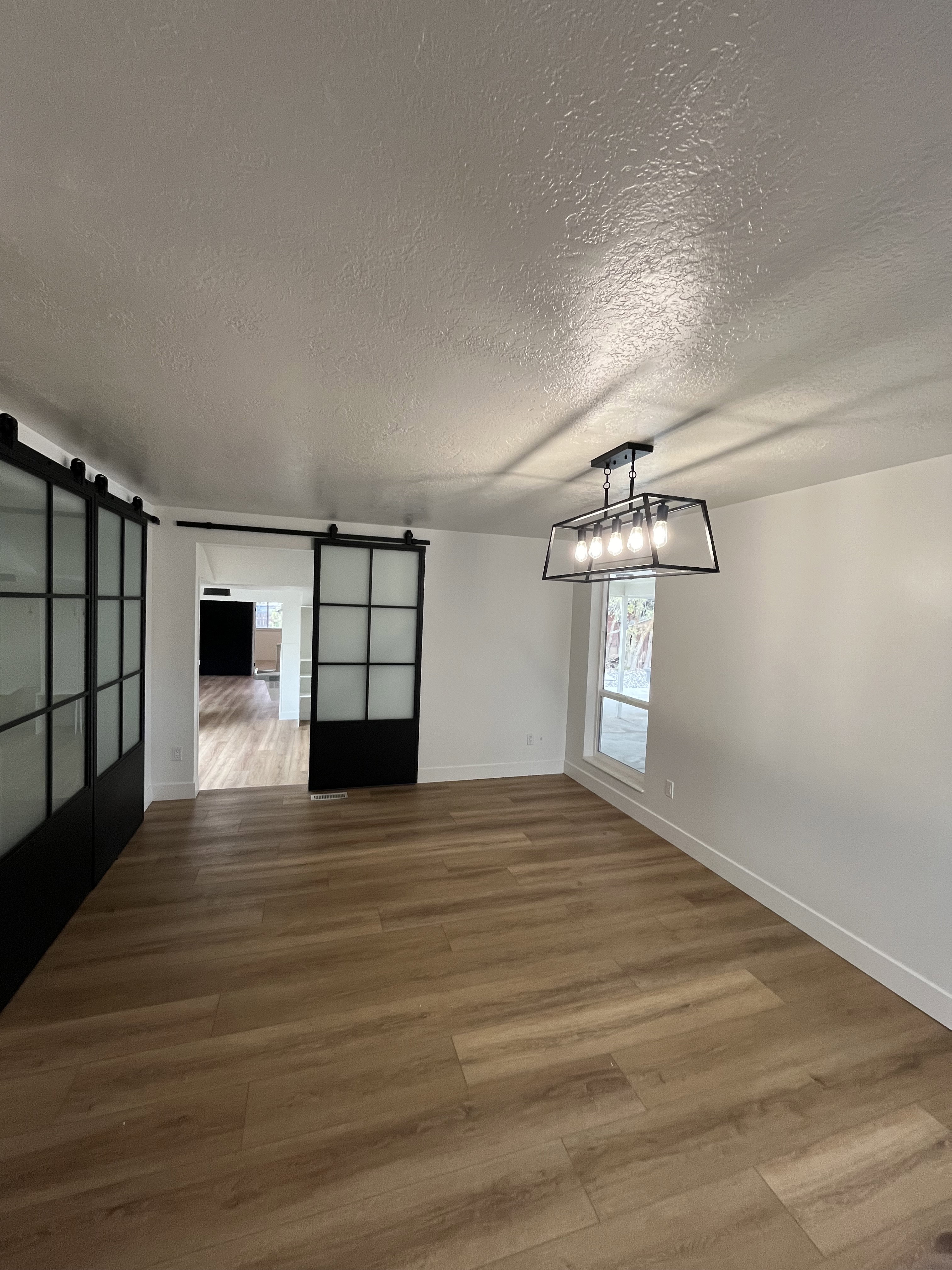 Spacious room featuring wood-finish flooring, white walls, and a contemporary linear chandelier with exposed bulbs