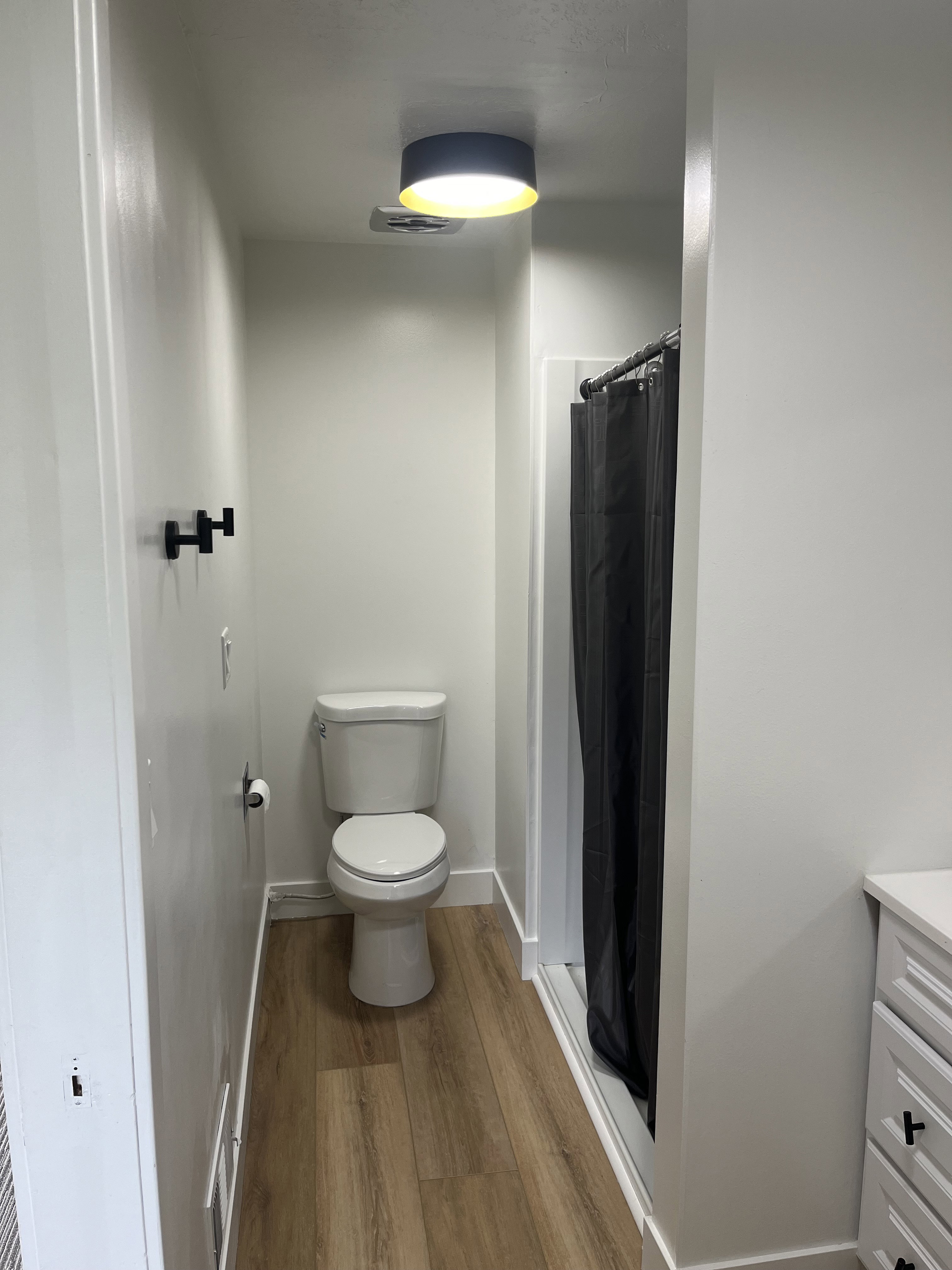 Bathroom with wood-finish flooring, a white toilet, and a stand-up shower with a dark shower curtain