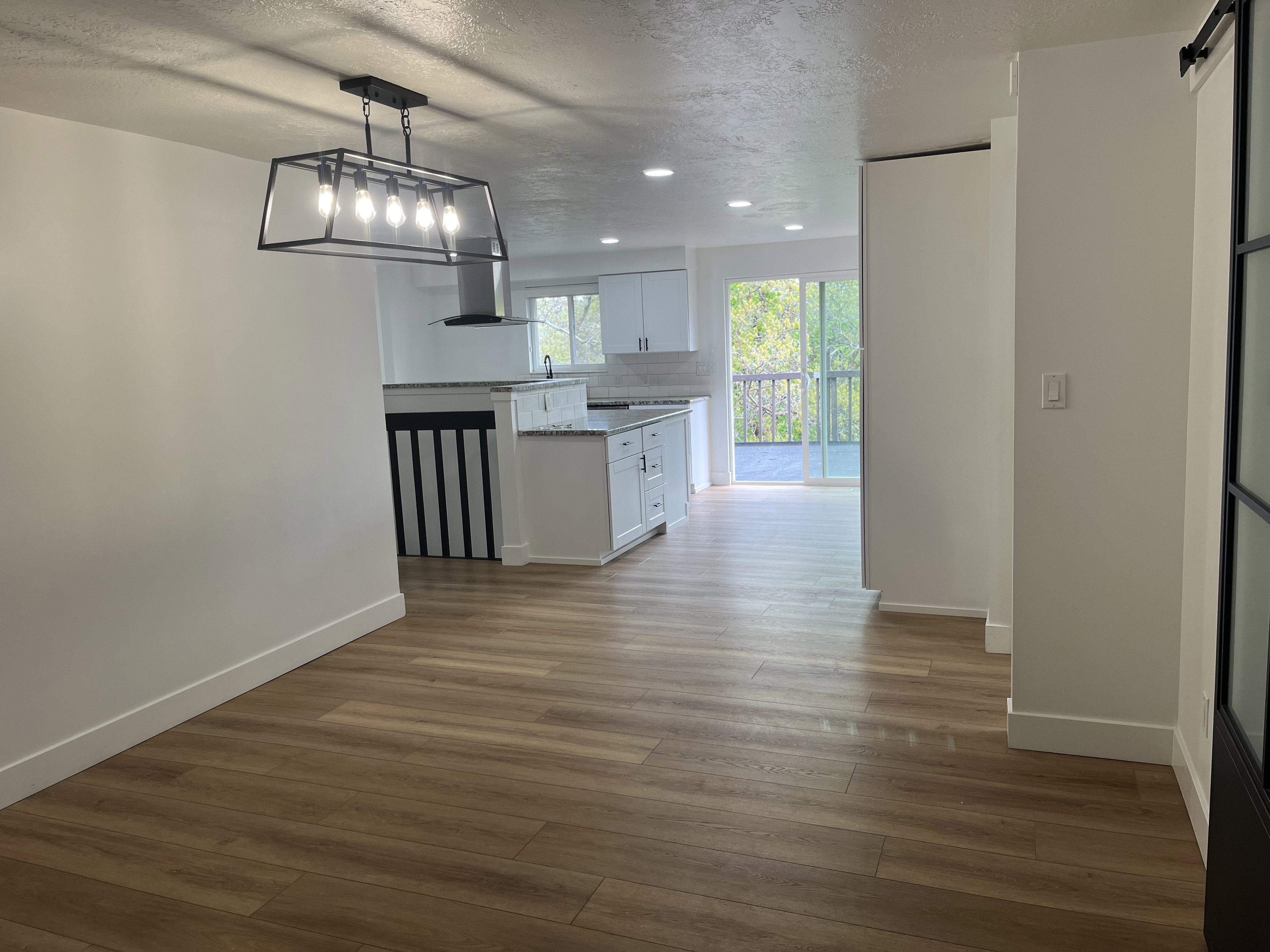 Open-concept living area featuring wood-finish flooring, a modern linear chandelier, recessed lighting, white baseboards, and a sliding glass door to an exterior deck
