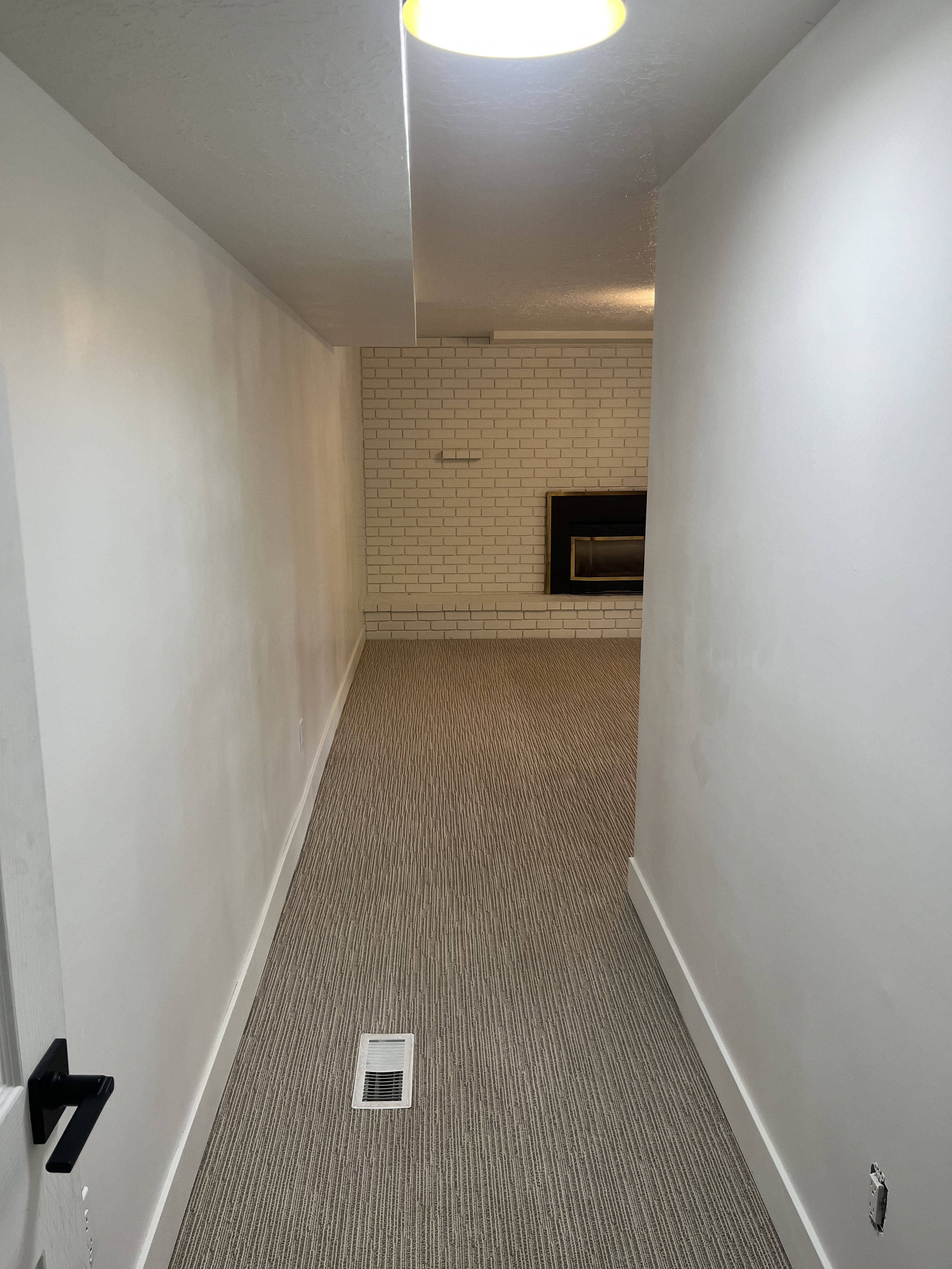 Recessed fireplace with a white painted brick surround, neutral carpet flooring, and white baseboards