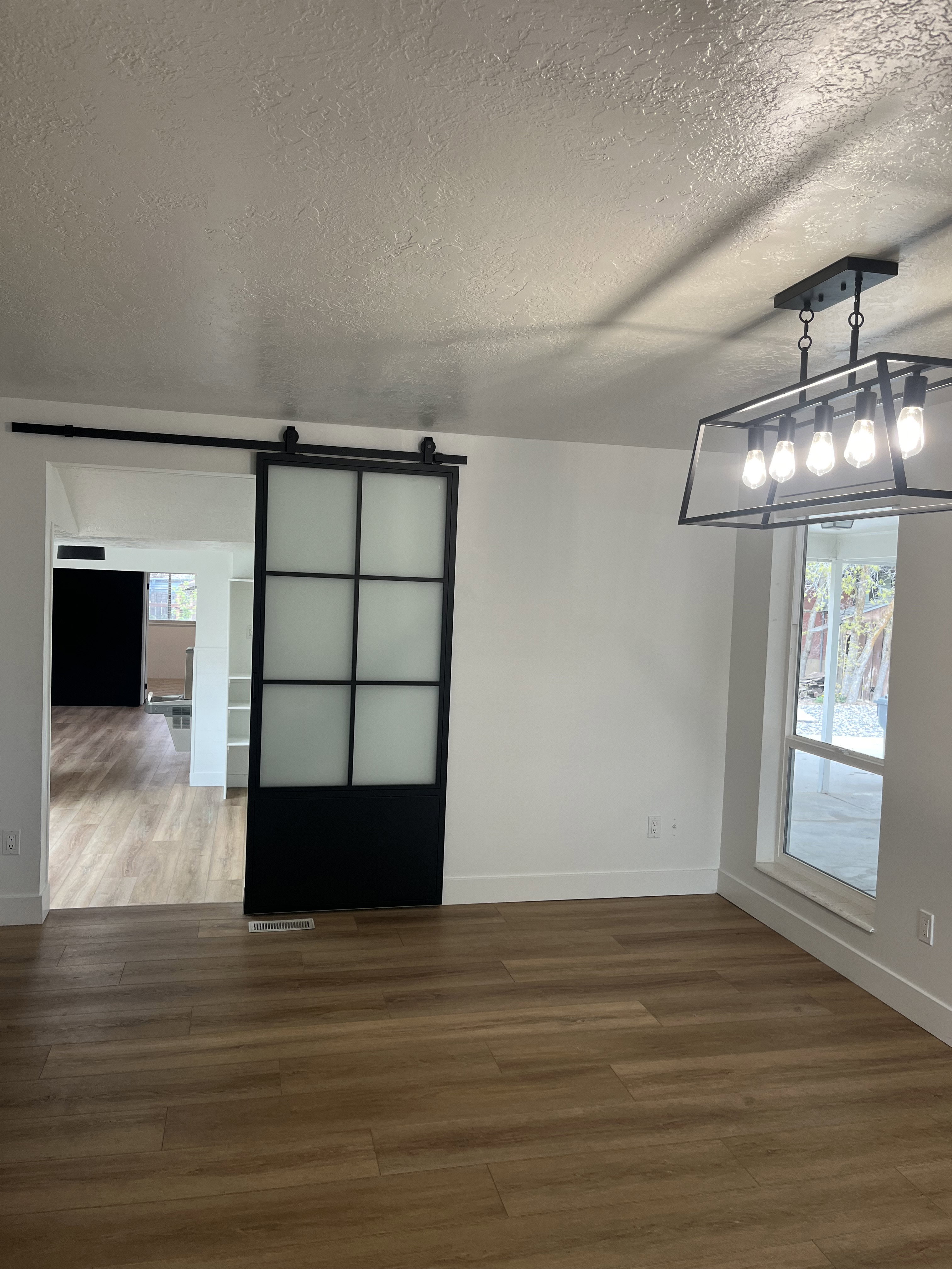 Spacious interior featuring wood-finish flooring, a modern linear chandelier, and a black framed barn door with frosted glass panels