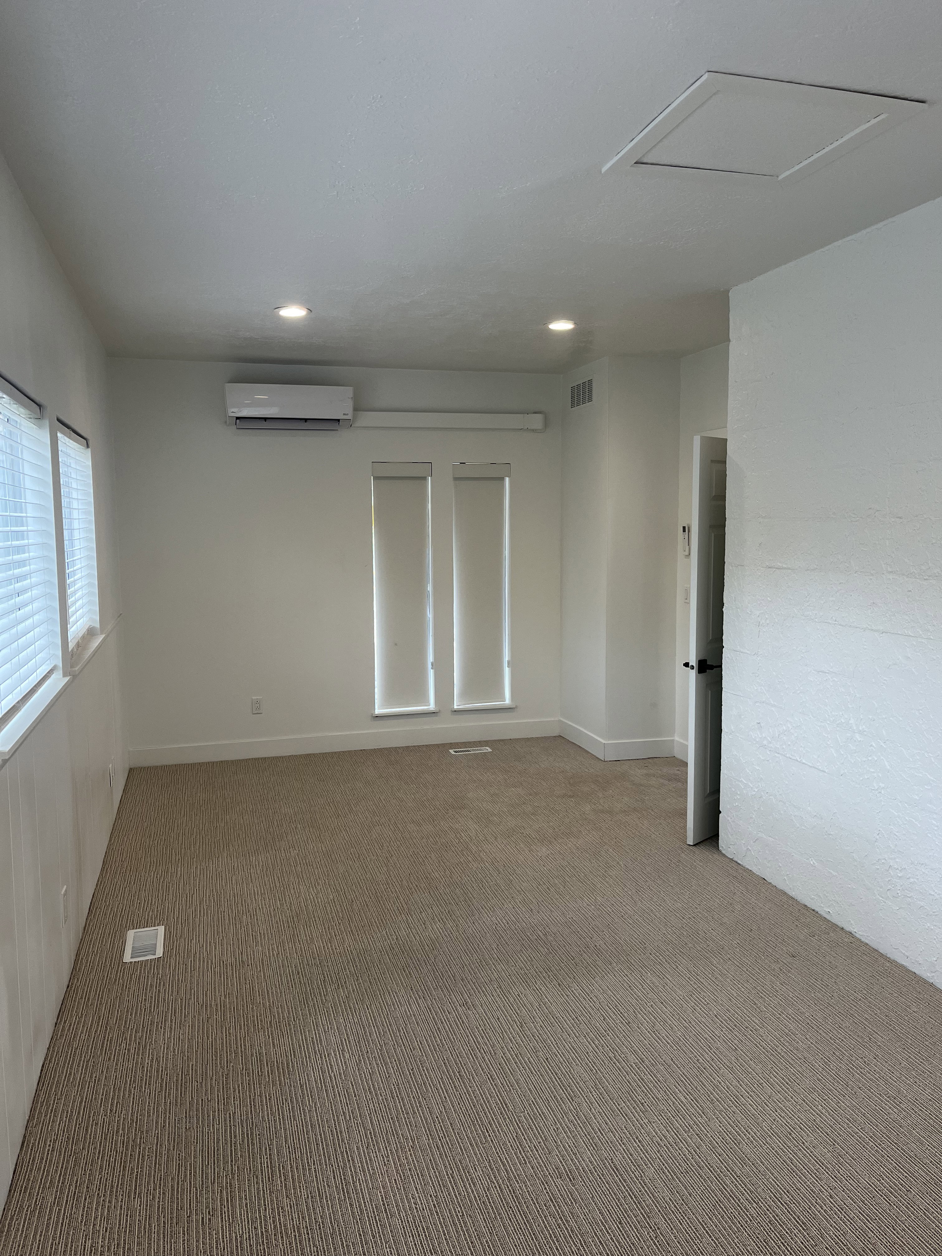 Carpeted room featuring recessed lighting, multiple windows with blinds, a wall-mounted air conditioning unit, and white baseboards