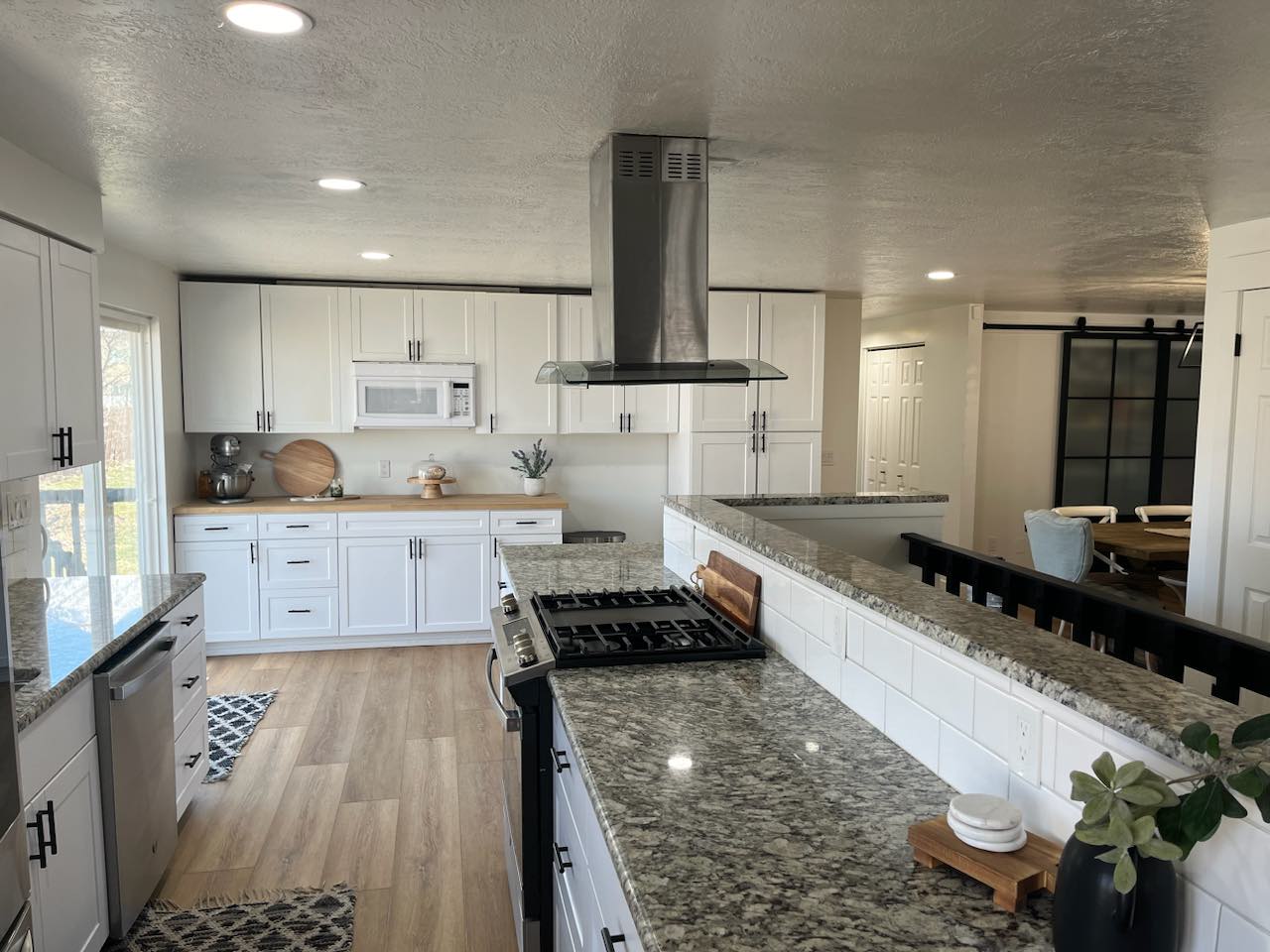 Modern kitchen featuring recessed lighting, white cabinetry with matte black hardware, wood-finish flooring, a stainless steel range hood, and granite countertops