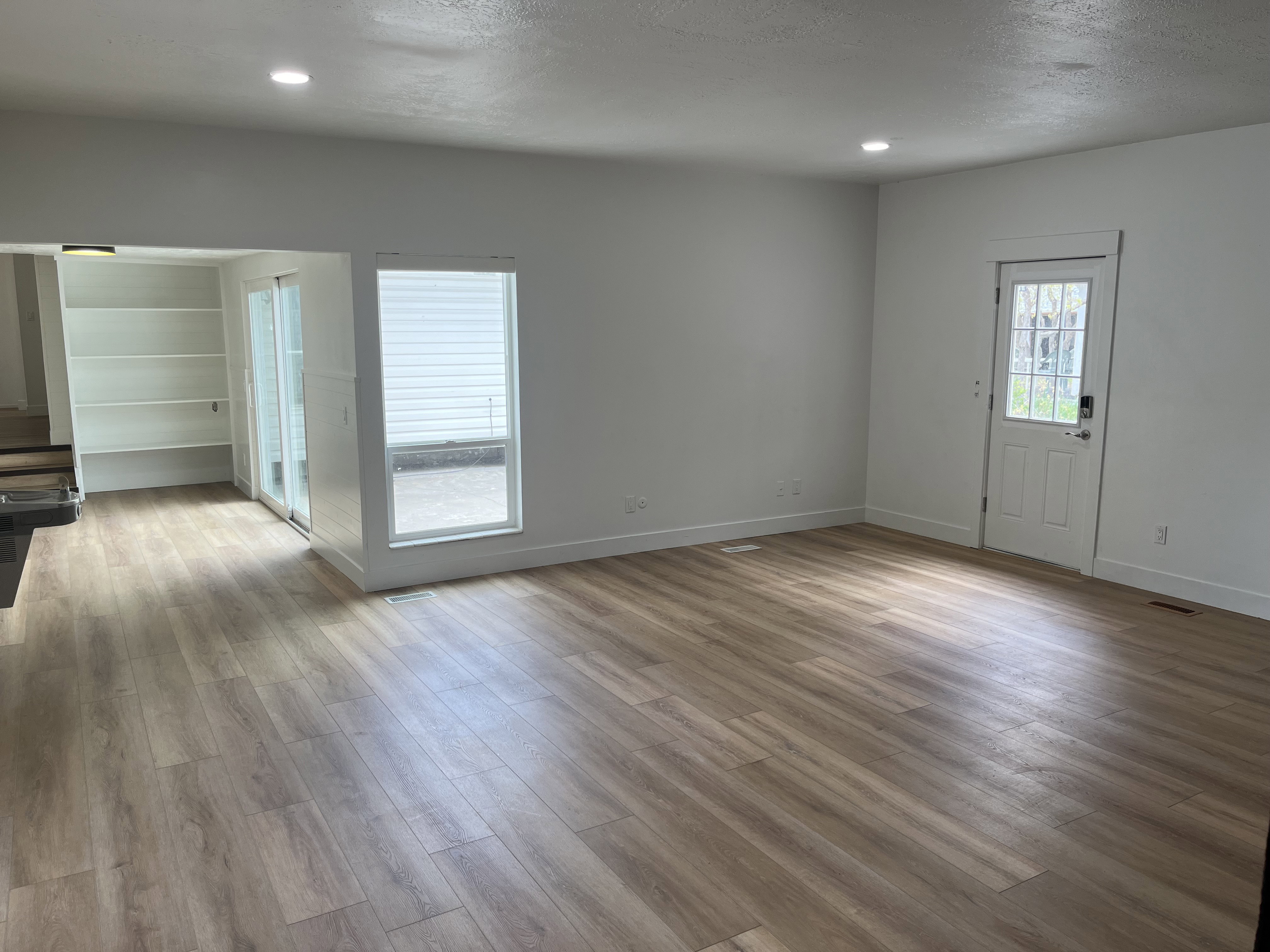 Spacious living area featuring wood-finish flooring, recessed lighting, and a white paneled entrance door