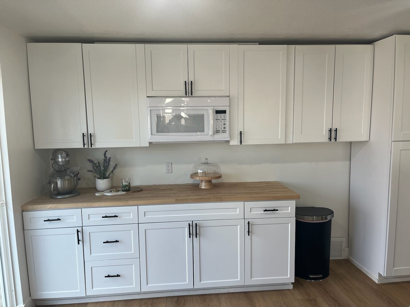 White shaker cabinetry with matte black hardware, wood-finish countertops, and an integrated microwave