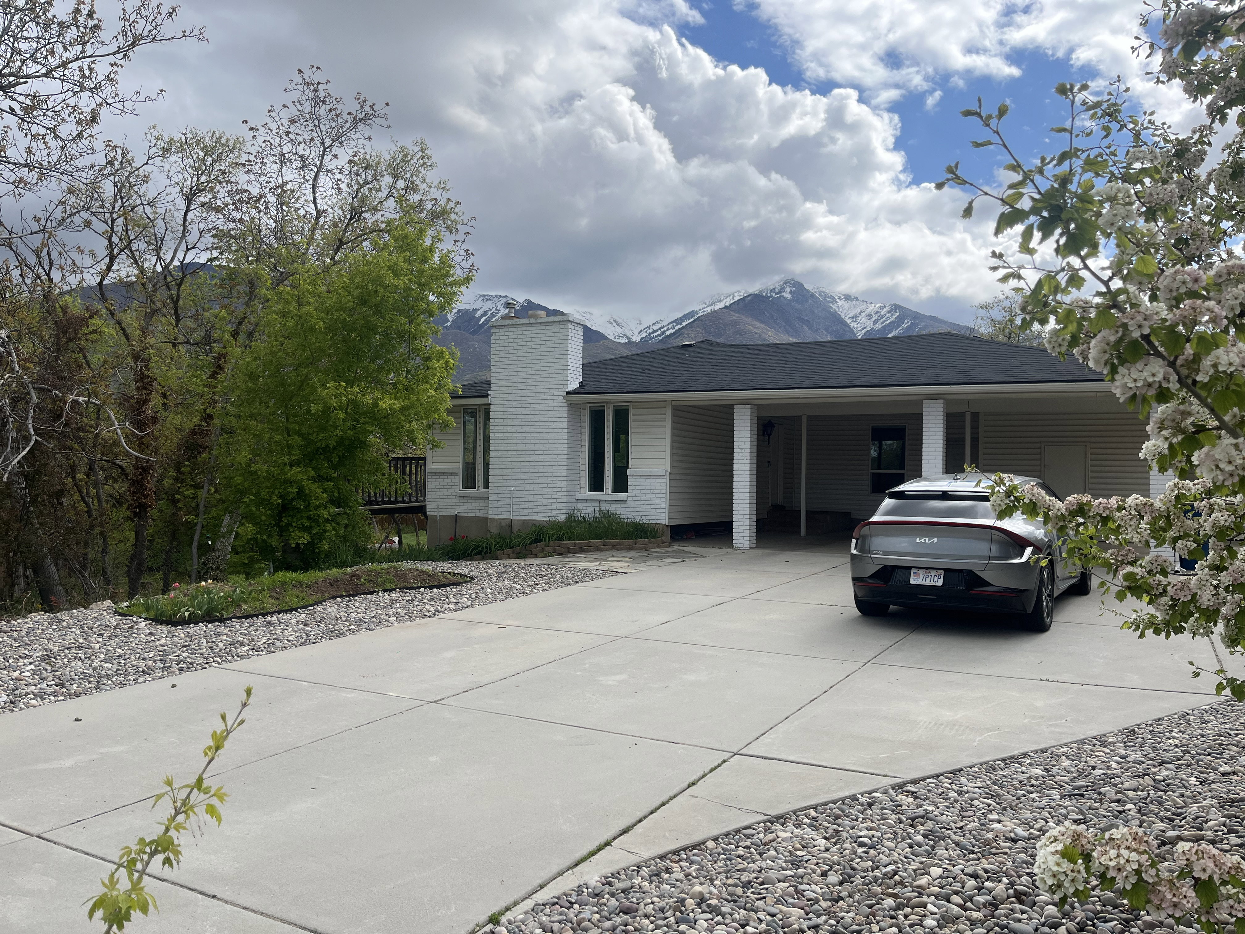 Contemporary single-story residence with a covered carport, expansive concrete driveway, and a newly installed dark shingle roof