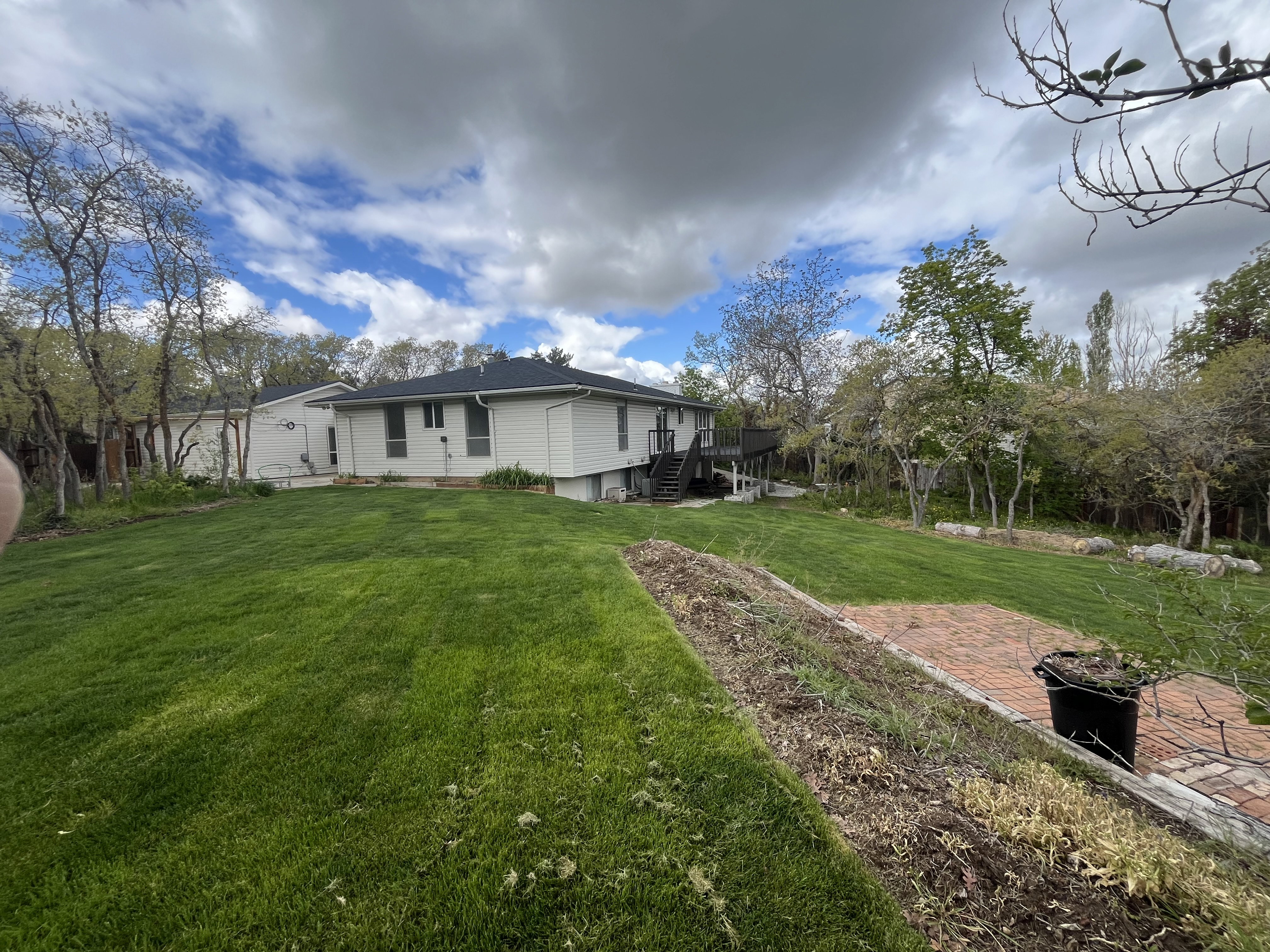 Expansive rear yard featuring a sloped lawn, a brick patio area, and a dark wood deck