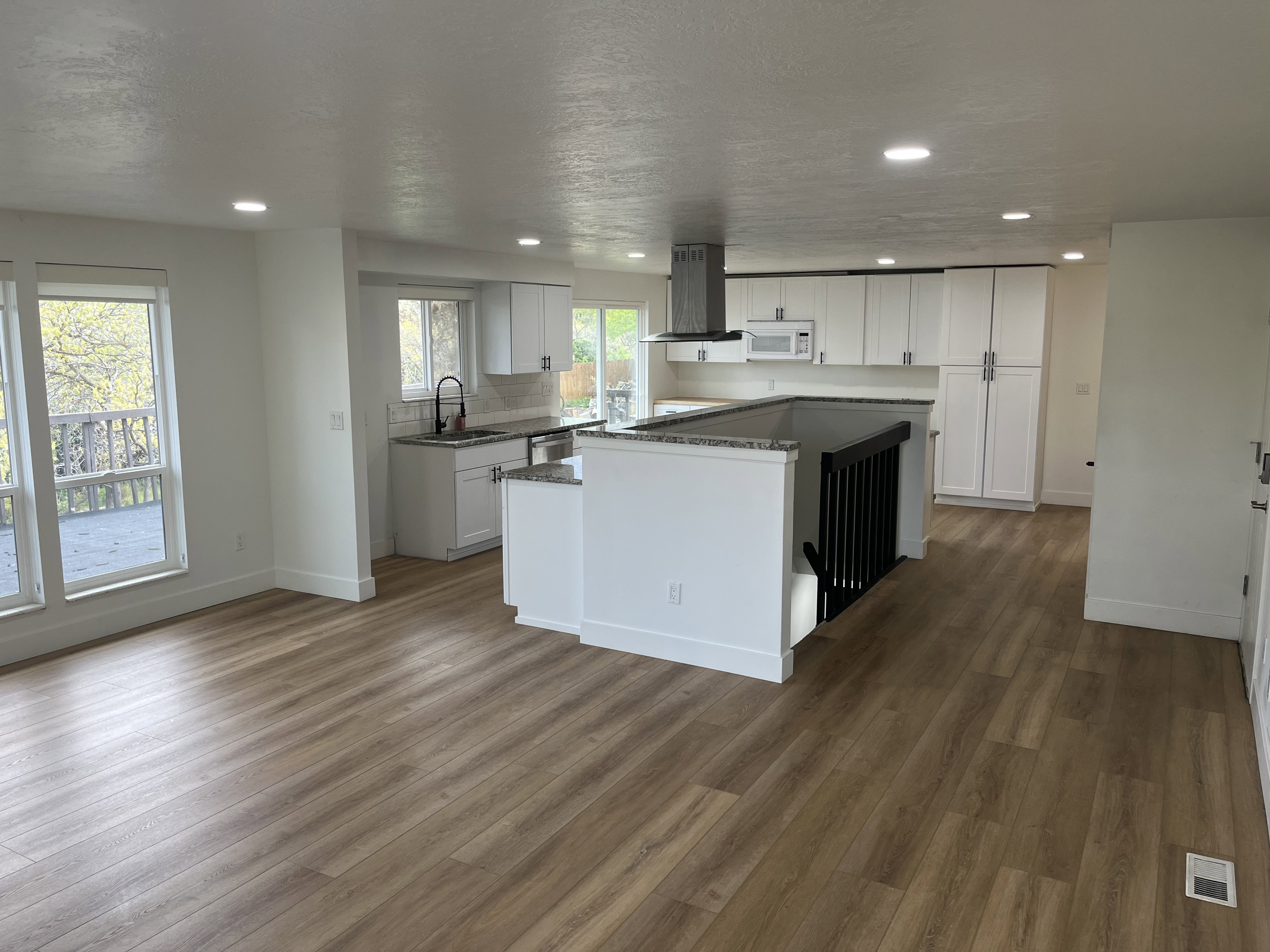 Open-concept kitchen and living area featuring wood-finish flooring, recessed lighting, and white cabinetry
