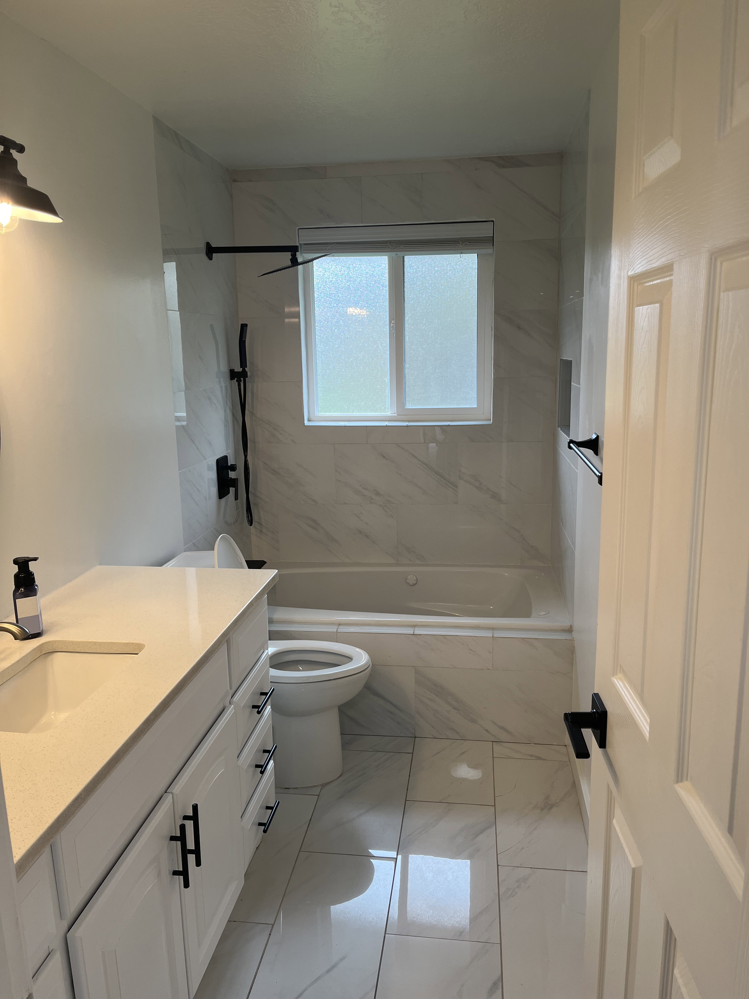 Contemporary bathroom featuring a white vanity with a light-toned countertop, a built-in bathtub with a shower, and a privacy window