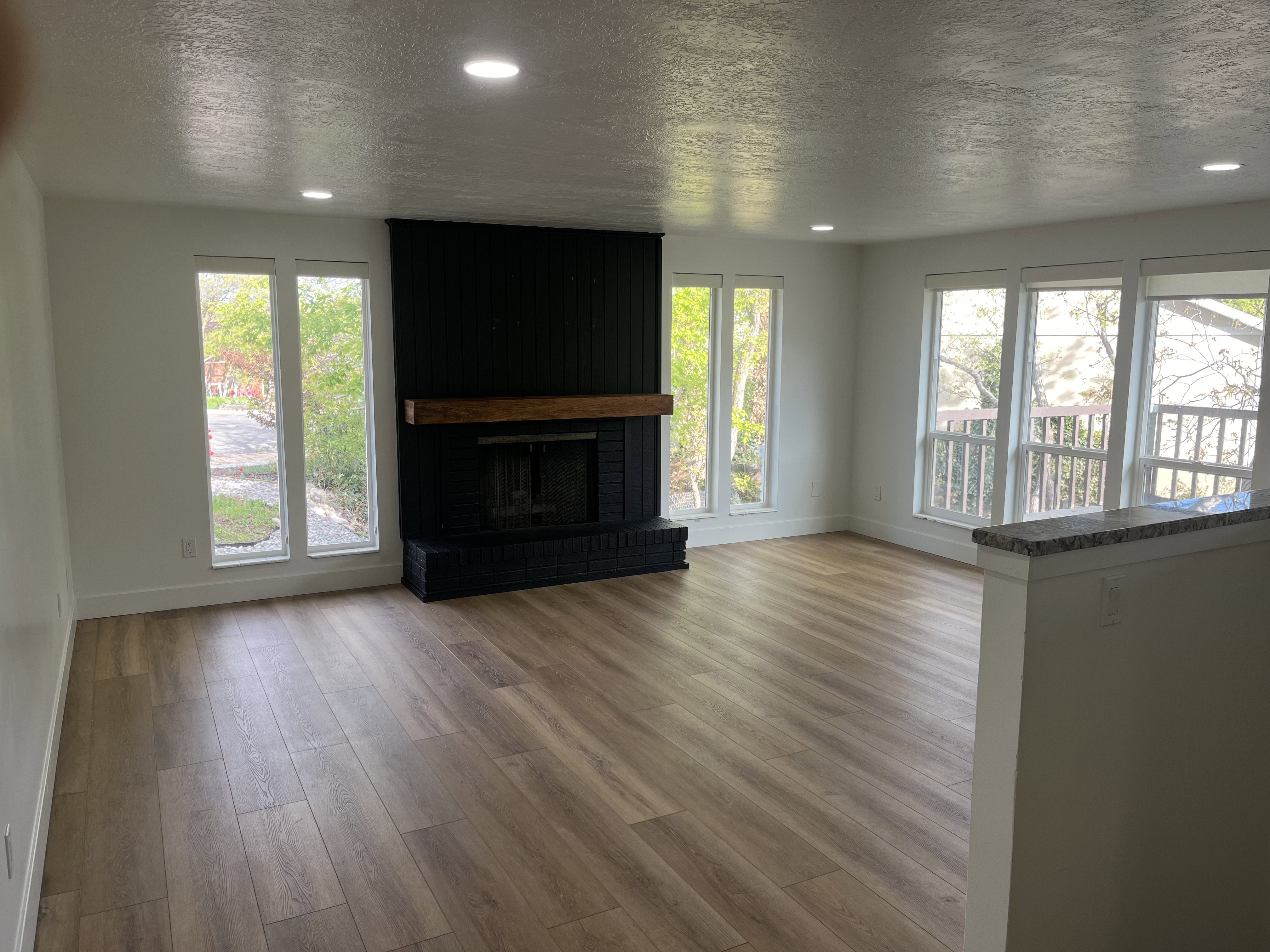 Spacious living area featuring a black brick fireplace with a wood mantel, wood-finish flooring, recessed lighting, and multiple large windows
