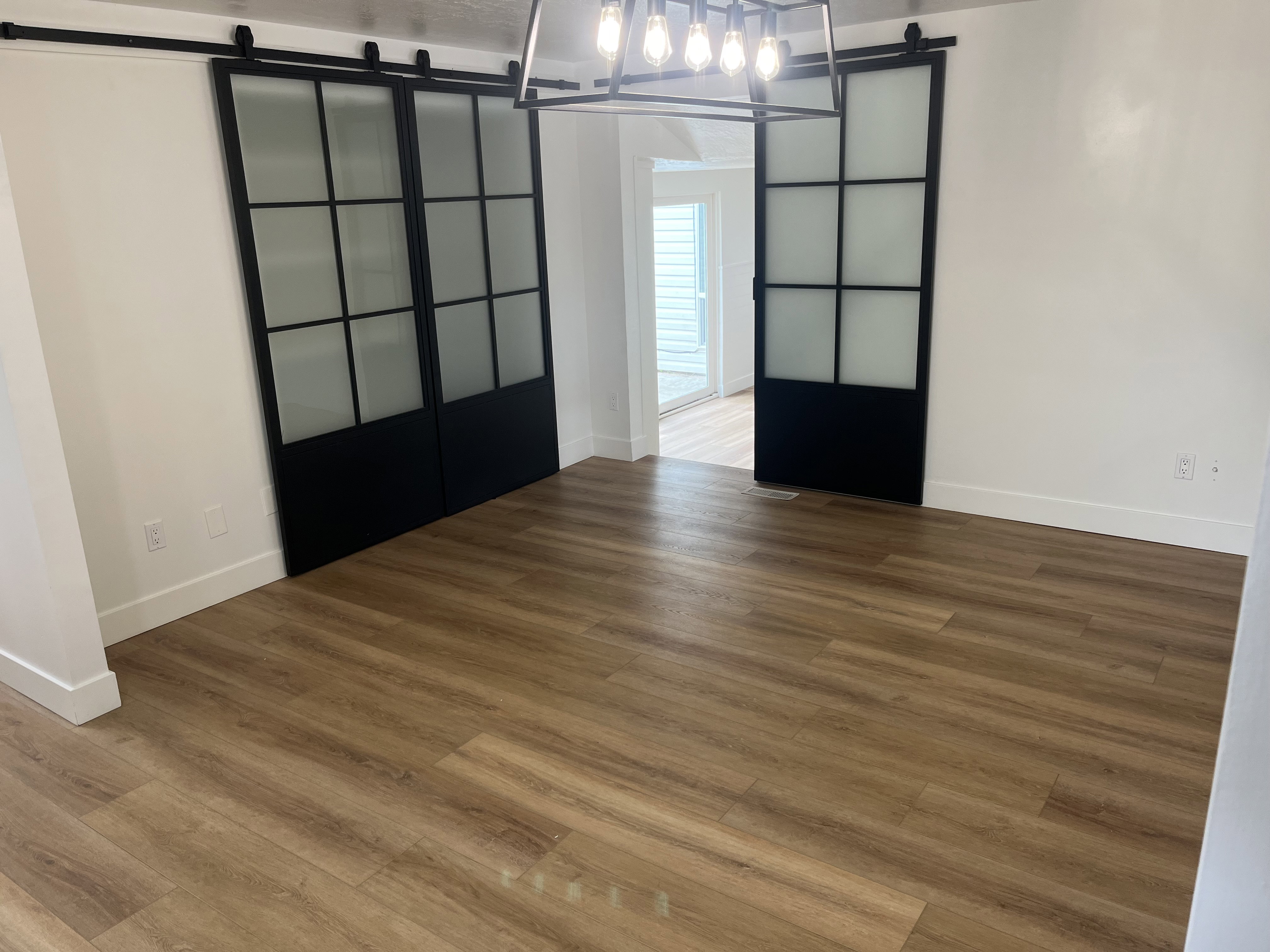 Spacious interior with wood-finish flooring, white baseboards, and a modern chandelier