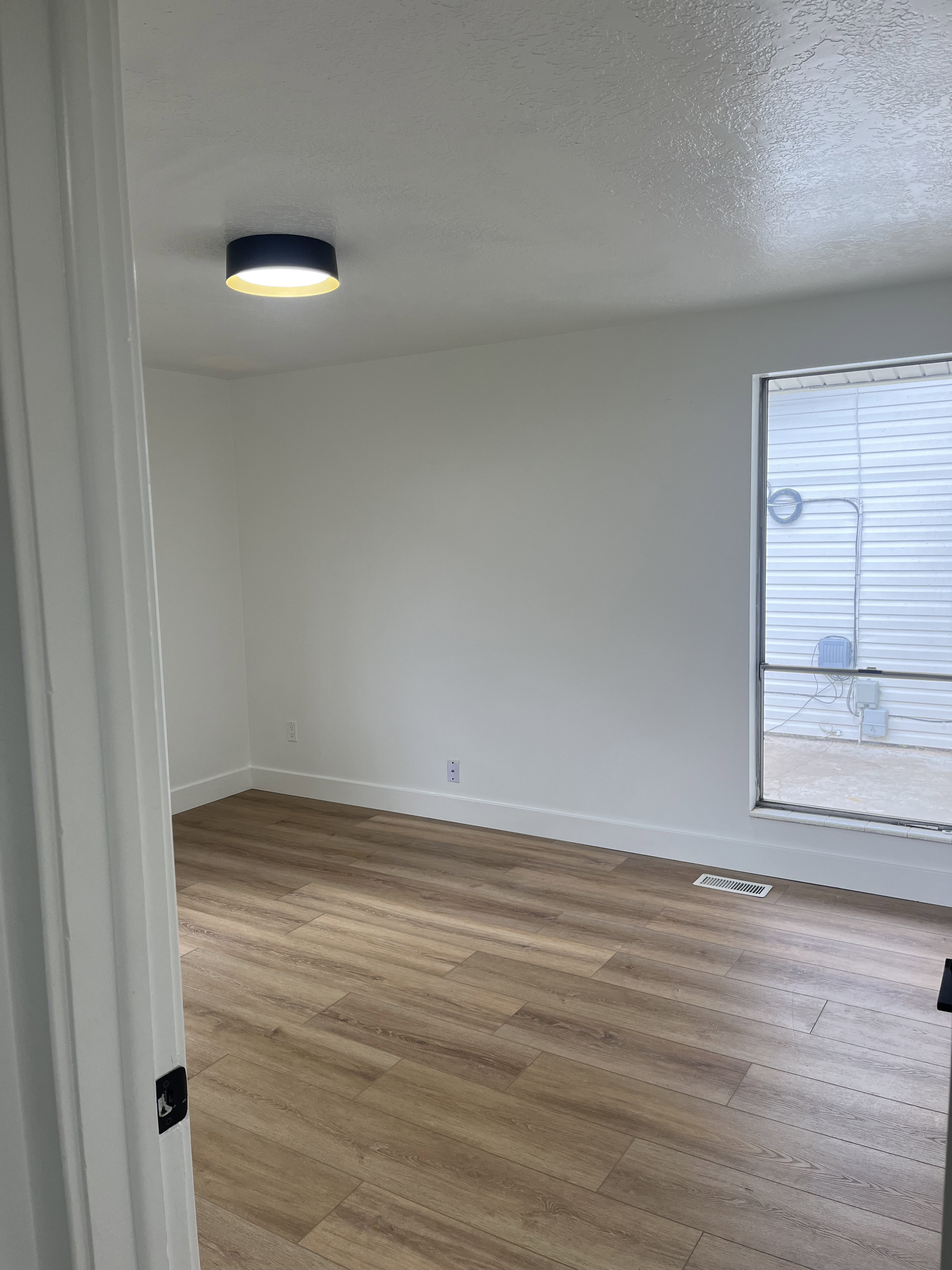 Spacious room featuring wood-finish flooring, white baseboards, and a modern flush-mount ceiling light