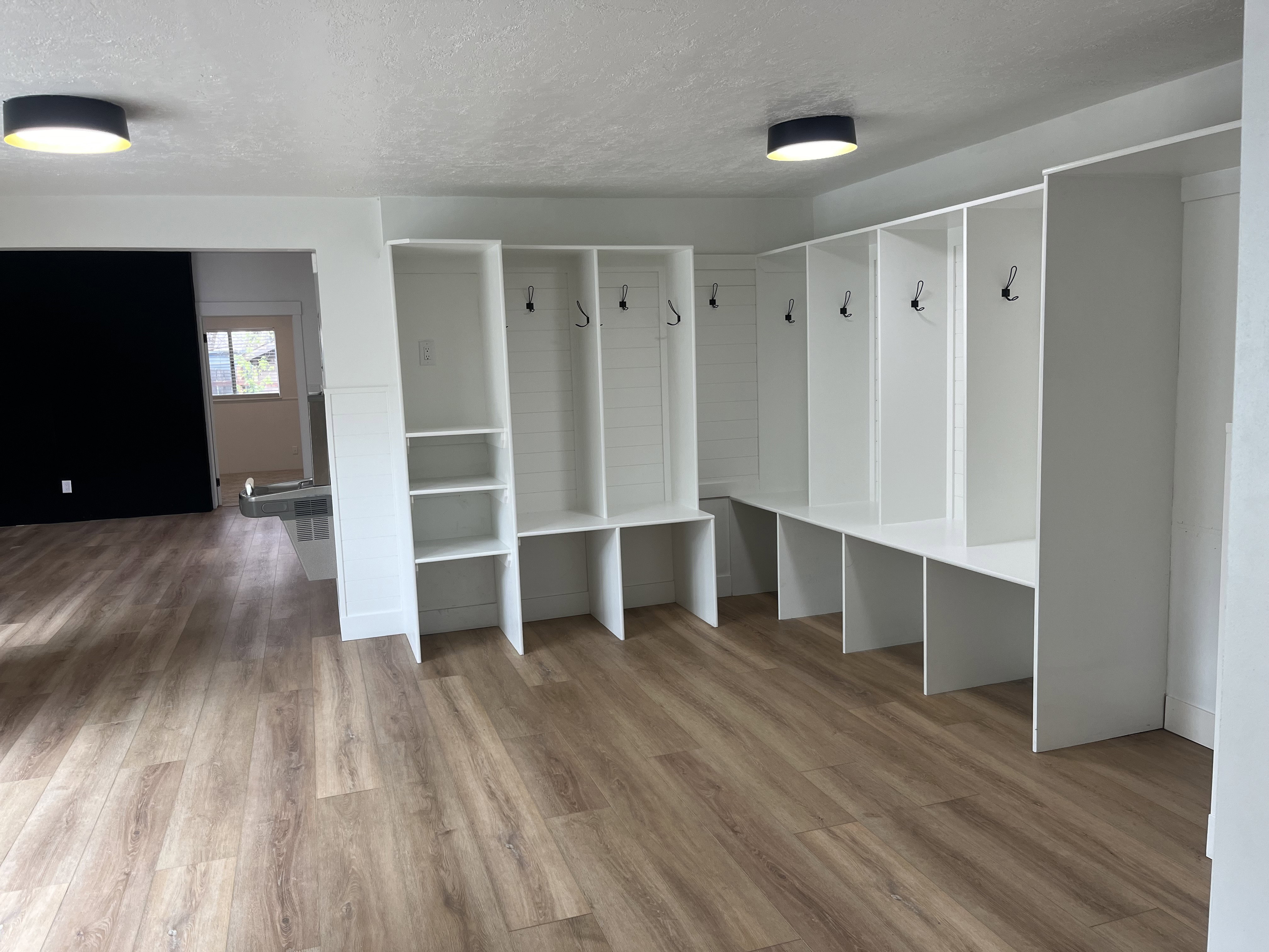 Built-in white storage lockers with integrated bench seating and shelving, wood-finish flooring, and contemporary flush-mount lighting fixtures