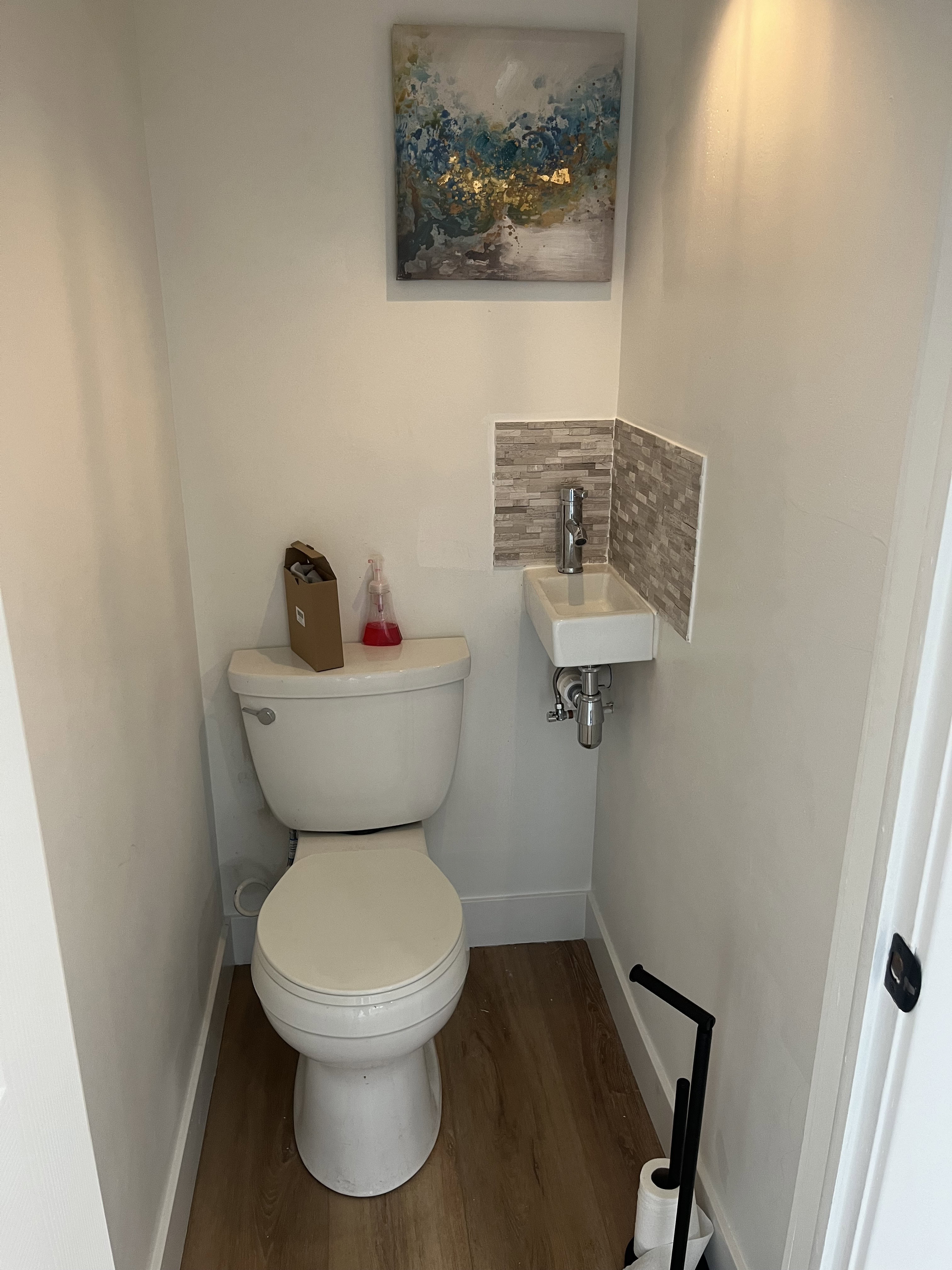Compact powder room featuring wood-finish flooring, a contemporary wall-mounted sink with chrome faucet, and a mosaic tile backsplash