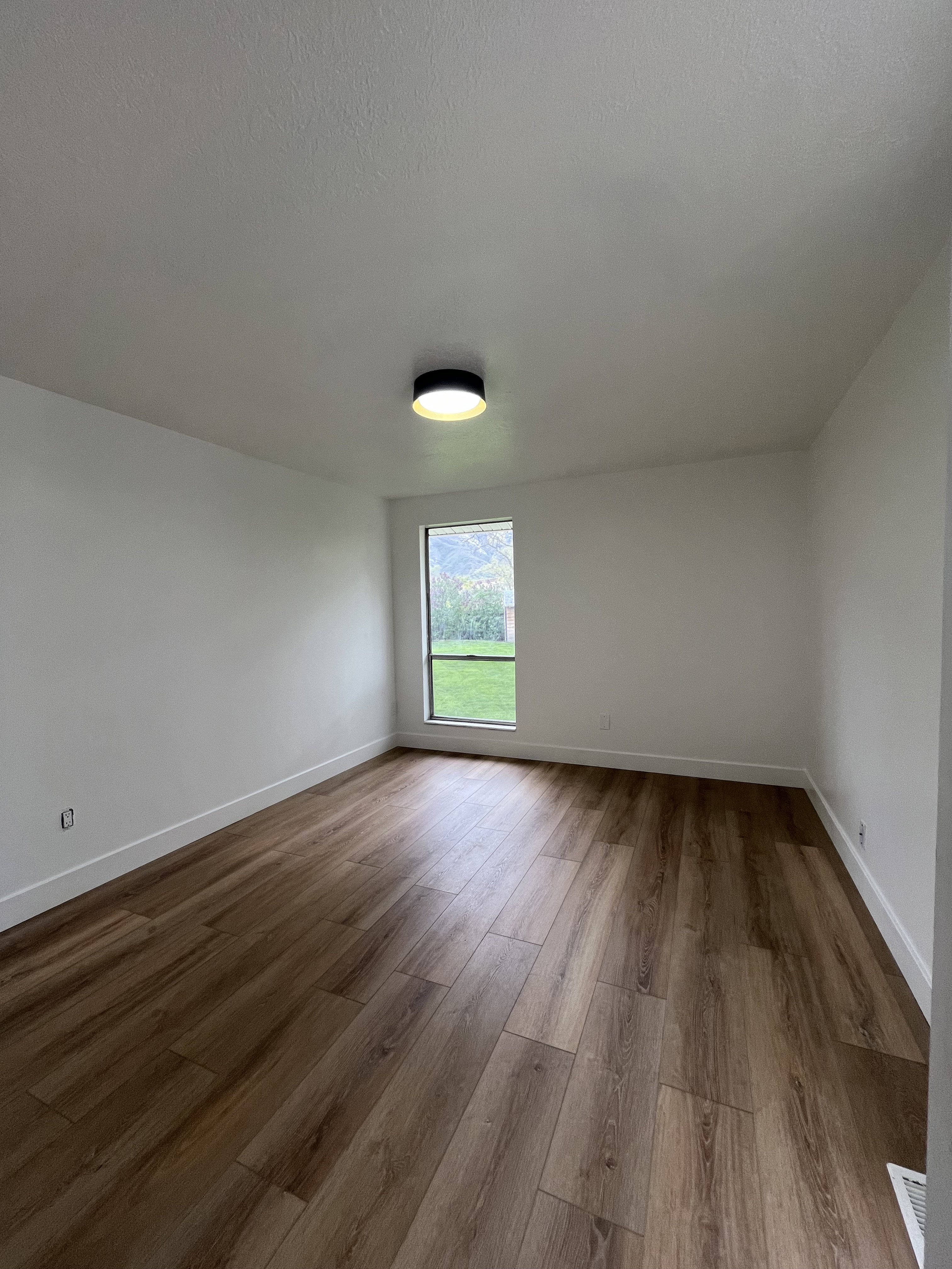 Spacious room featuring wood-finish flooring and crisp white baseboards