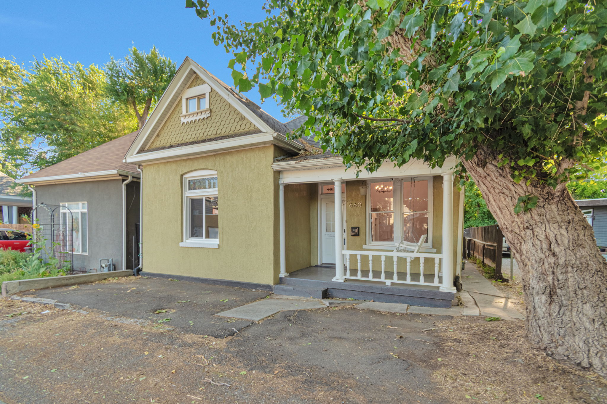 Charming bungalow featuring a distinct gabled roofline with decorative shingles, a covered porch with white railing, and a vibrant green exterior facade