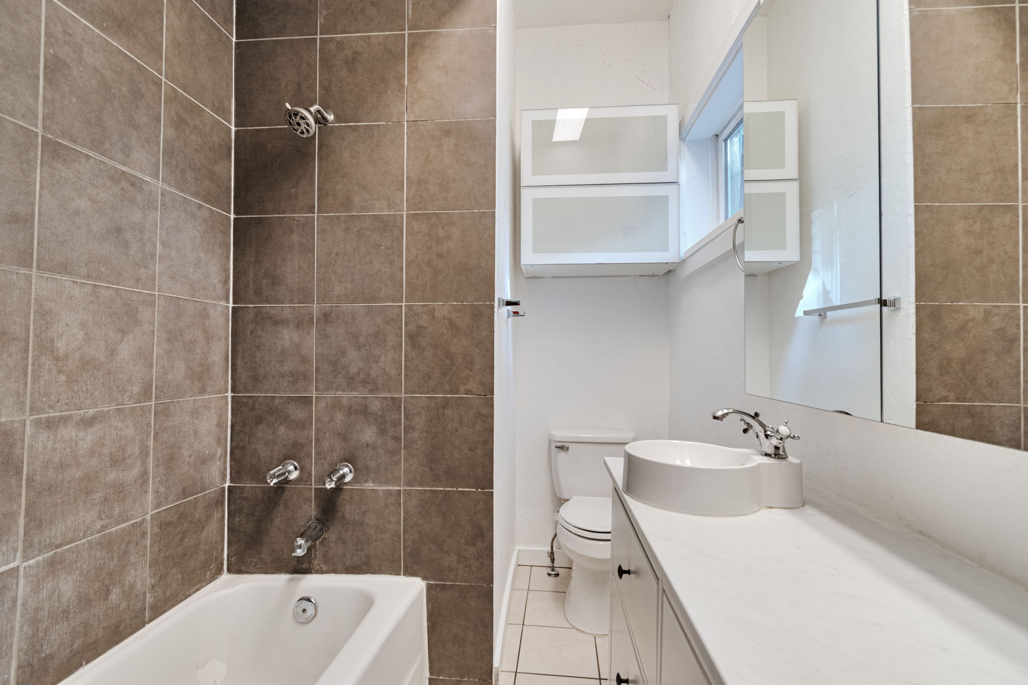 Full bathroom featuring a white bathtub, brown tiled shower surround, white vanity with an integrated vessel sink, and a large wall-mounted mirror