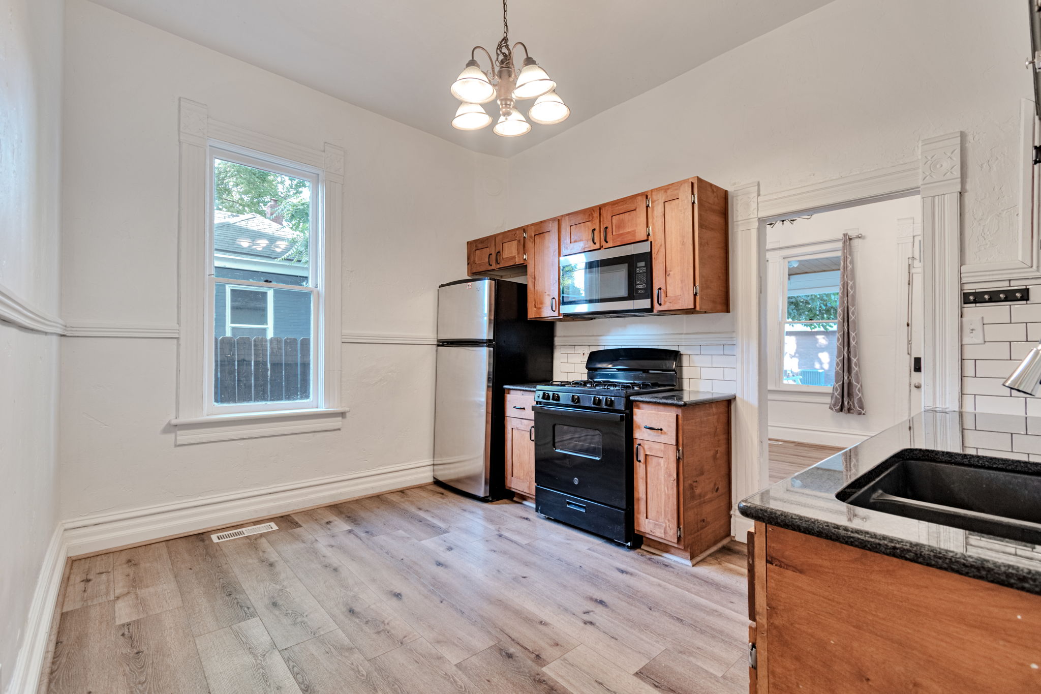 Kitchen featuring wood-finish flooring, wood cabinetry, subway tile backsplash, and dark countertops