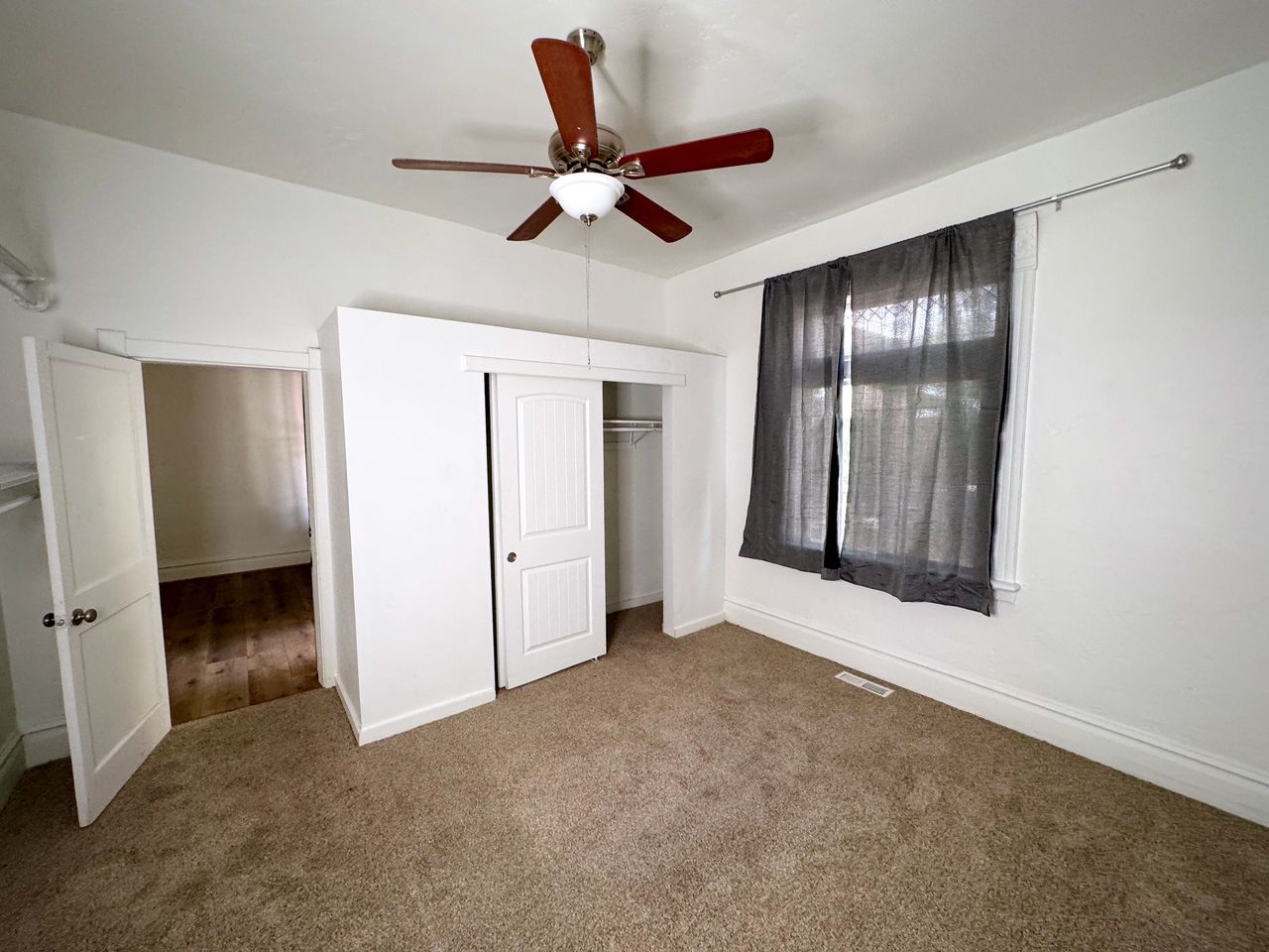 Carpeted room with a ceiling fan, a window, and a built-in closet with sliding doors