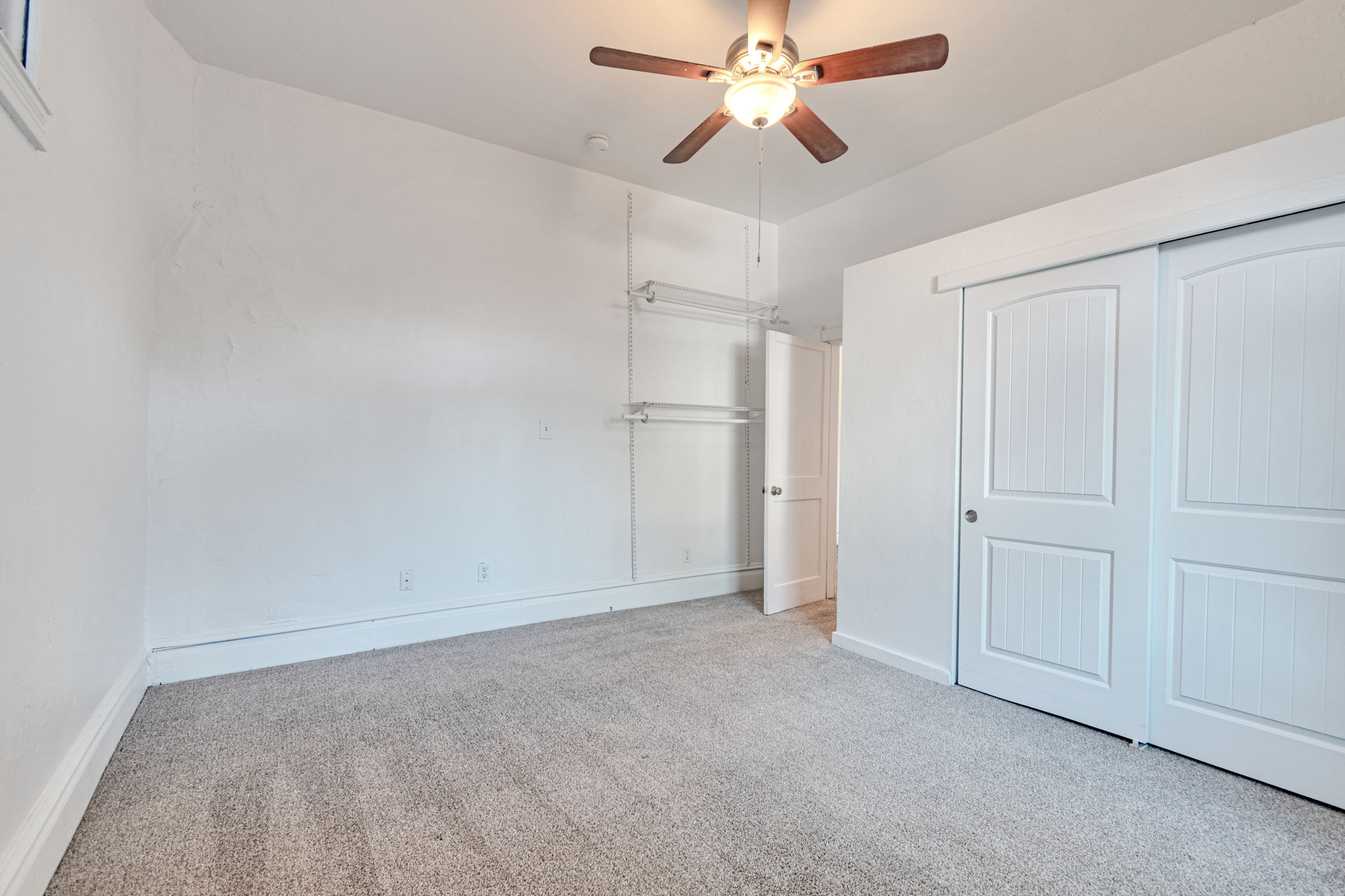 Carpeted room with white walls, wood-finish ceiling fan, and white sliding closet doors