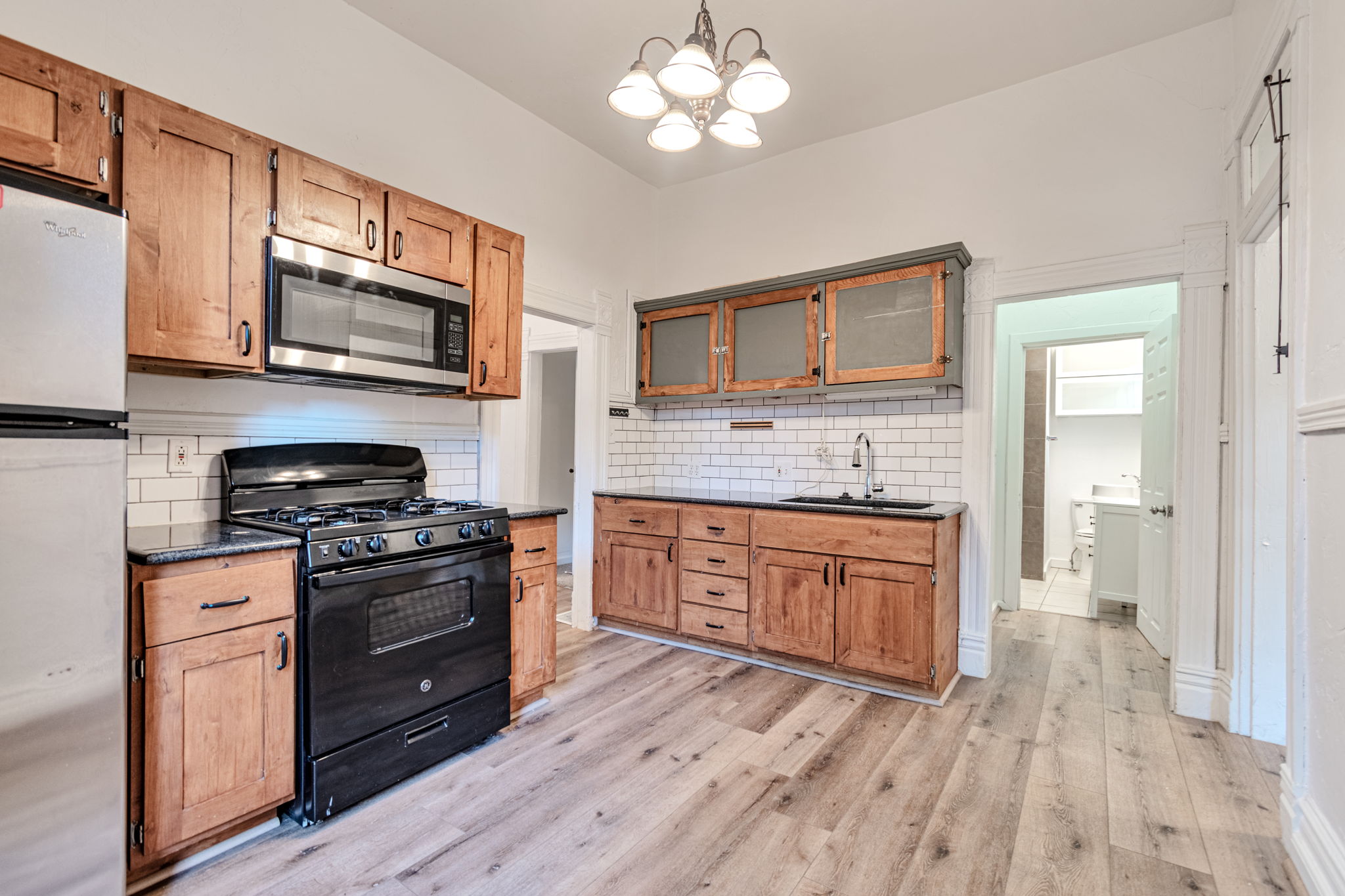 Kitchen featuring wood cabinetry, stainless steel microwave, black range, and wood-finish flooring