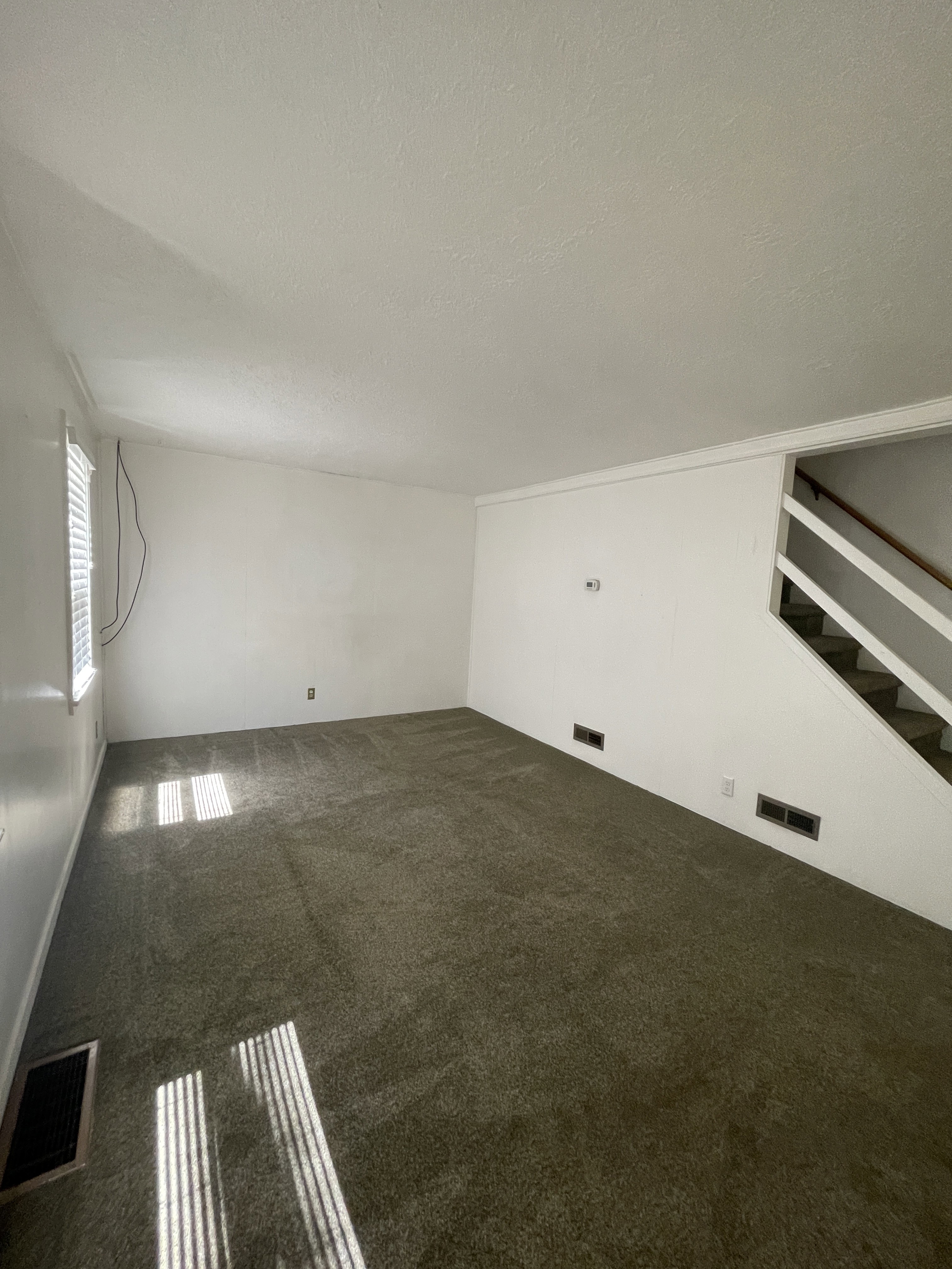Spacious room featuring neutral carpeting, white walls, and a staircase with open risers
