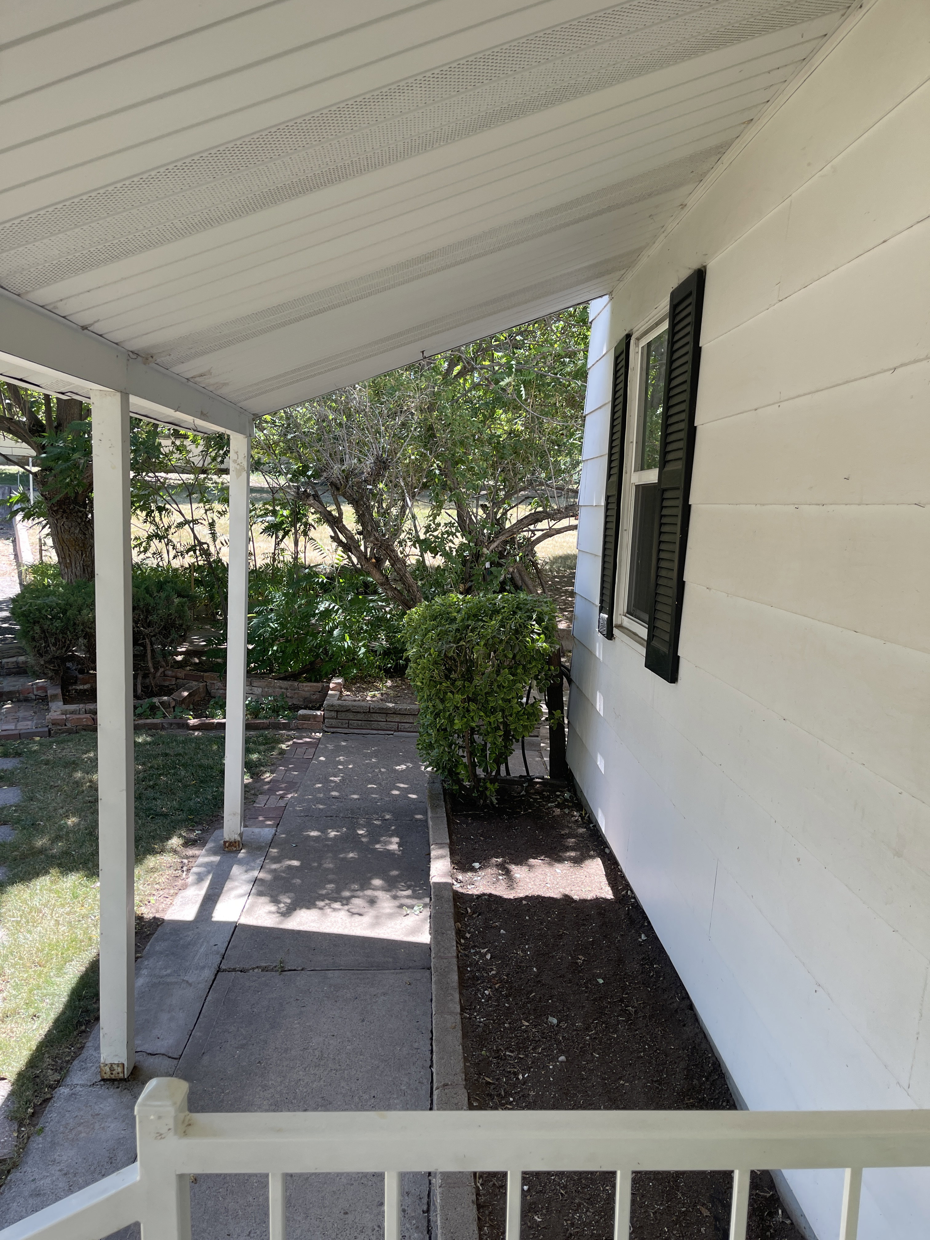 Covered porch with white siding exterior and black louvered shutters