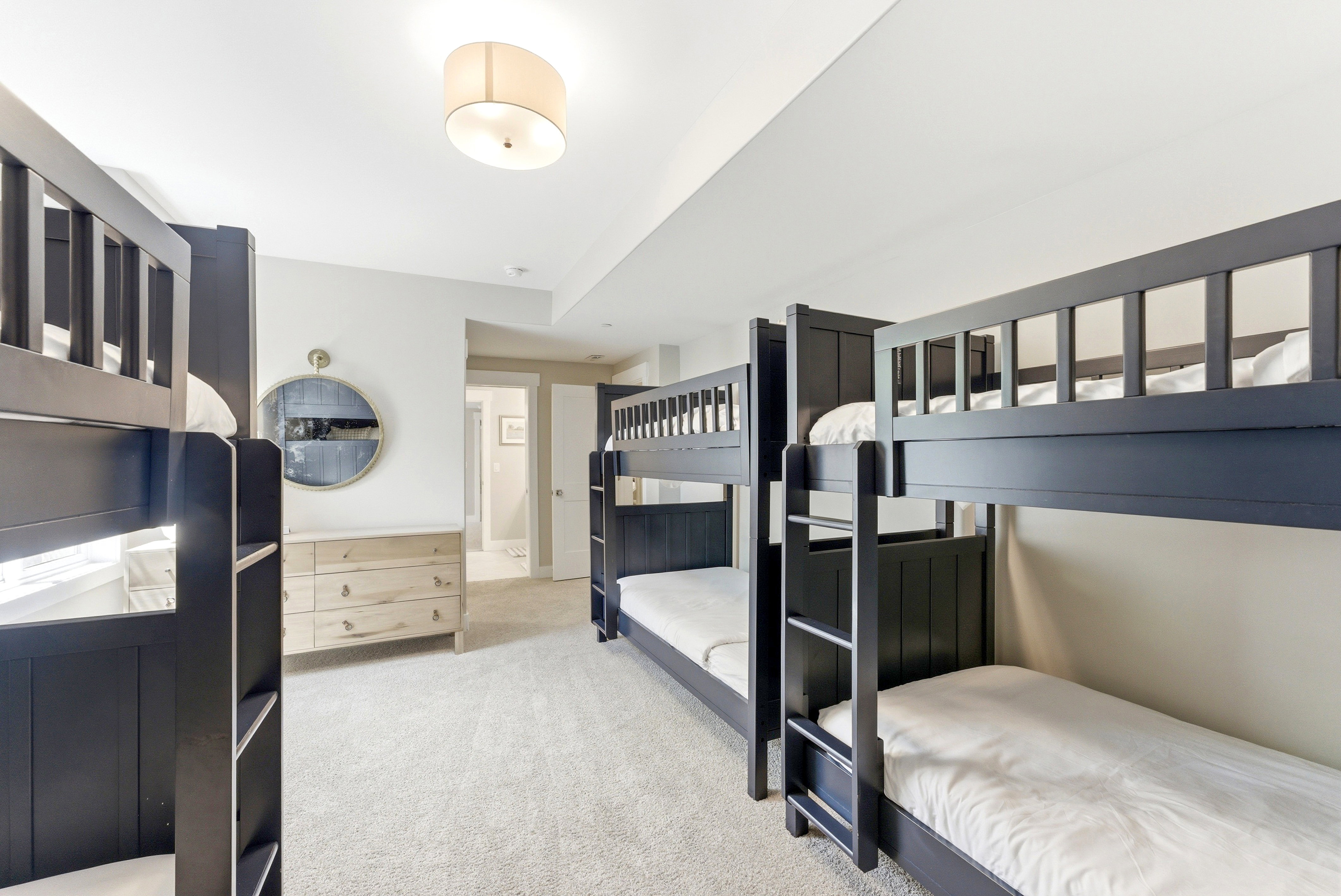 Spacious room featuring multiple dark-stained bunk beds, light-colored carpeting, and a ceiling-mounted drum light fixture