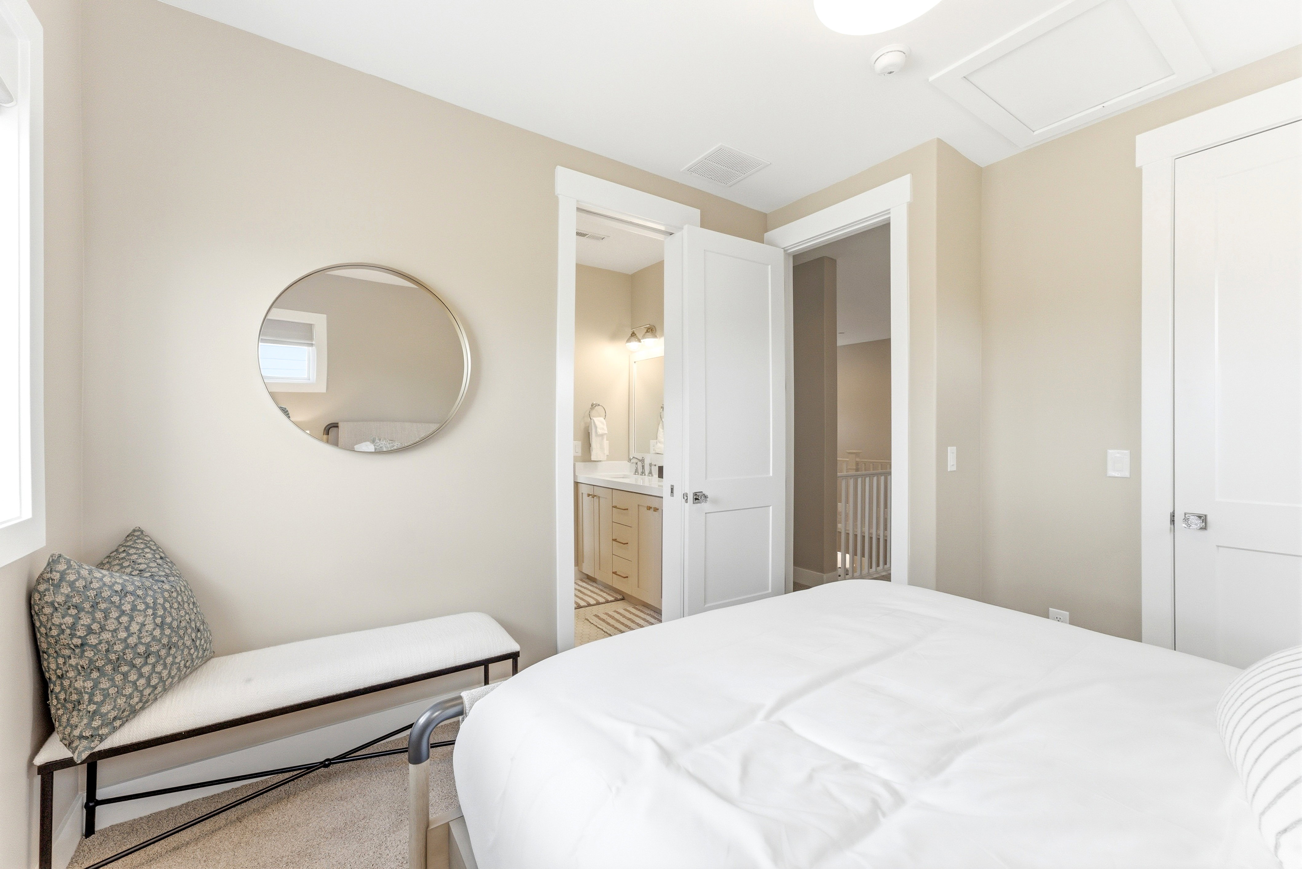 Bedroom with light beige wall paint and white trim, featuring a round wall mirror, a window with white casing, and carpeting