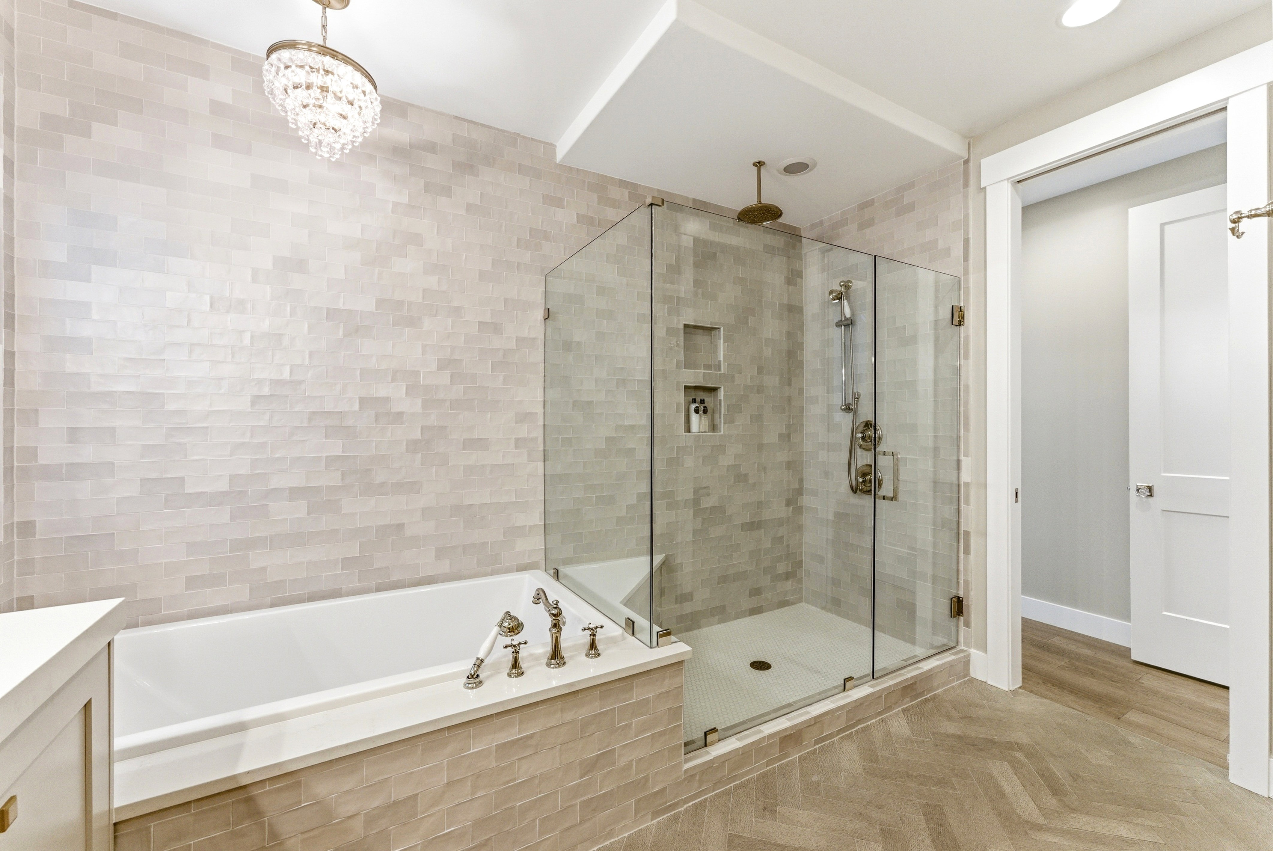 Bathroom featuring a frameless glass shower enclosure with dual shower heads, a built-in soaking tub with a handheld shower, herringbone-patterned floor tiling, and a crystal chandelier