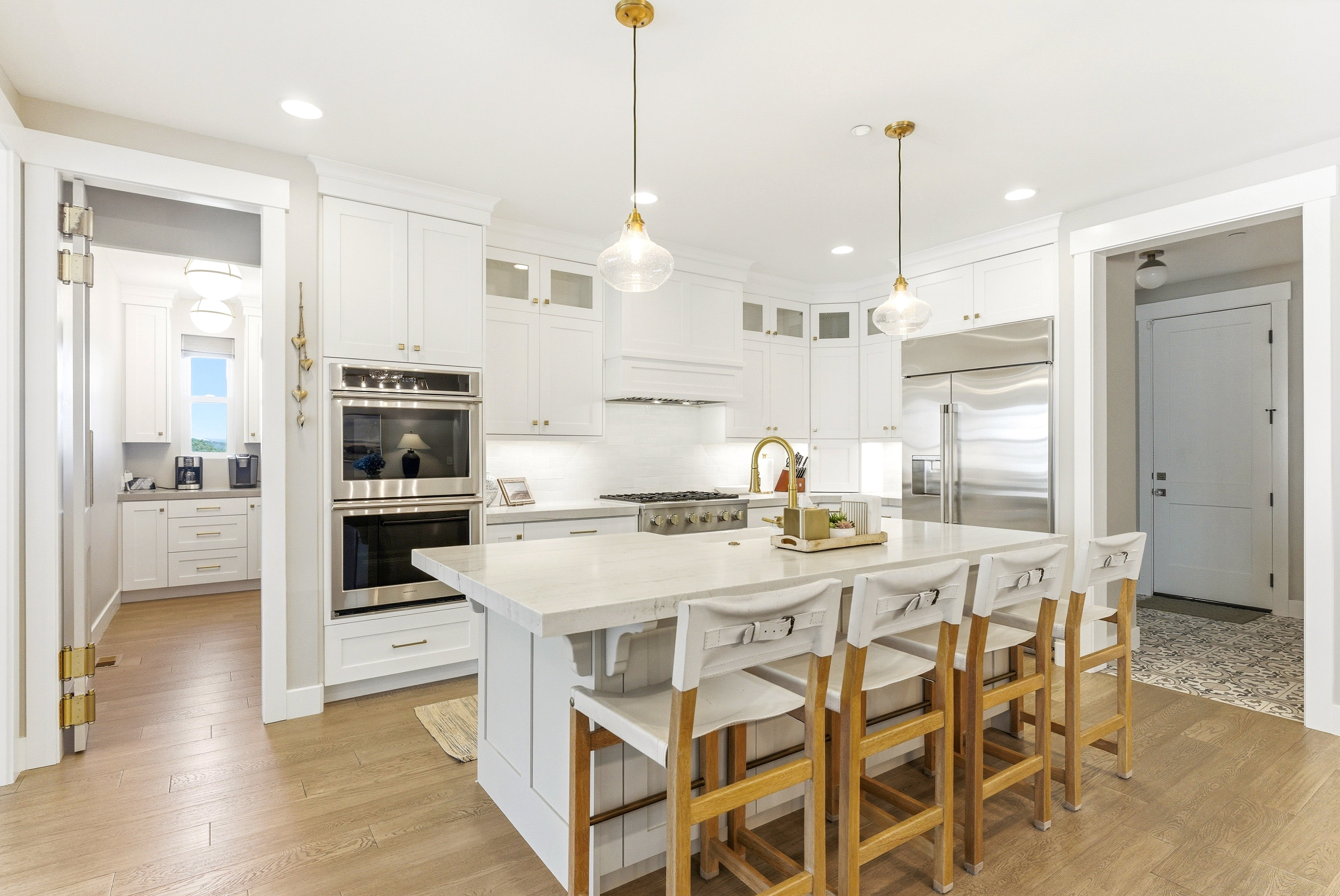 Expansive kitchen featuring white cabinetry, stainless steel appliances, a large center island with seating, a gas range, and wood-finish flooring