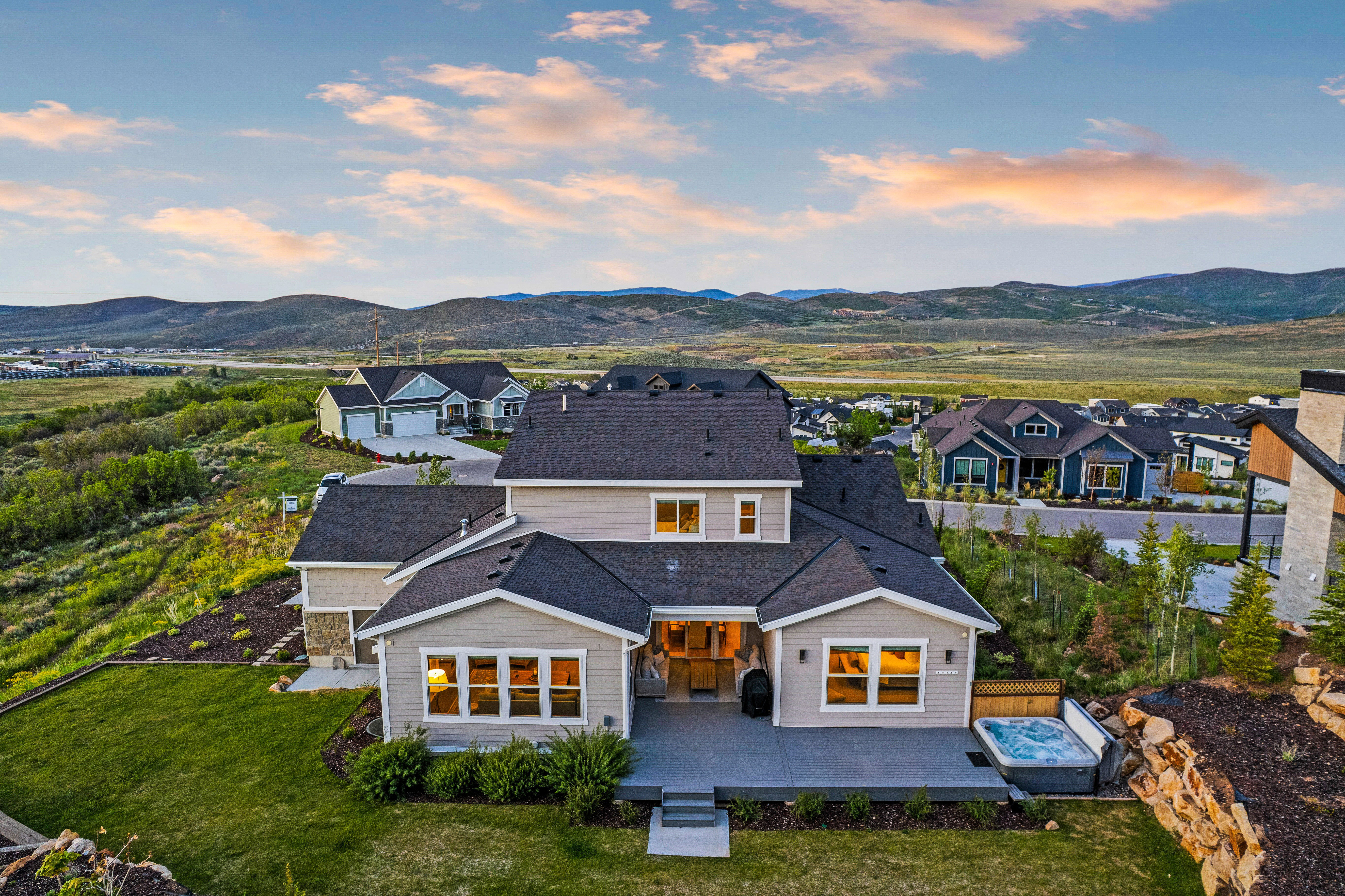 Rear exterior featuring a spacious concrete patio, integrated hot tub, and a tiered rock retaining wall
