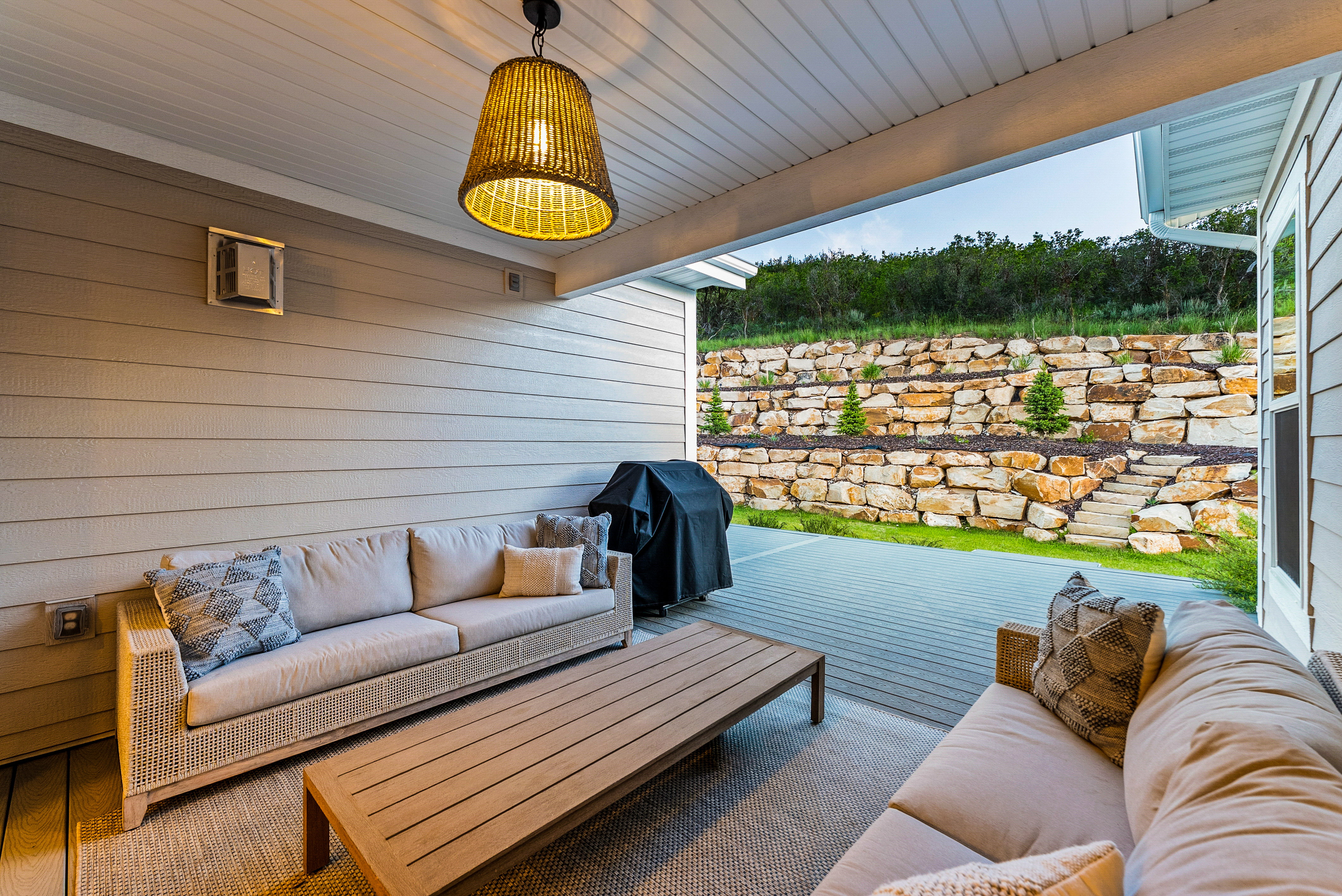 Covered patio featuring a wood-finish ceiling, woven pendant light, and a stone retaining wall with integrated plantings