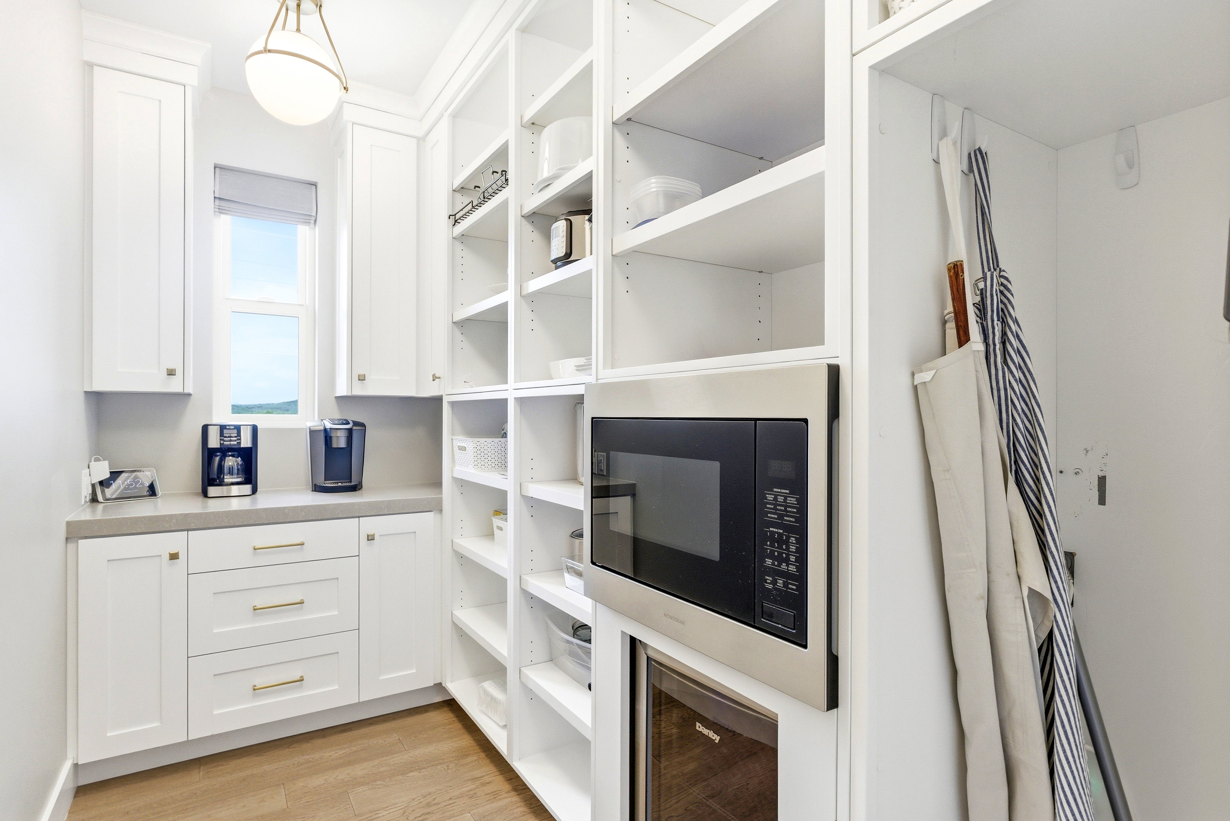 Bright utility space featuring white cabinetry, a built-in microwave, a beverage cooler, and extensive shelving