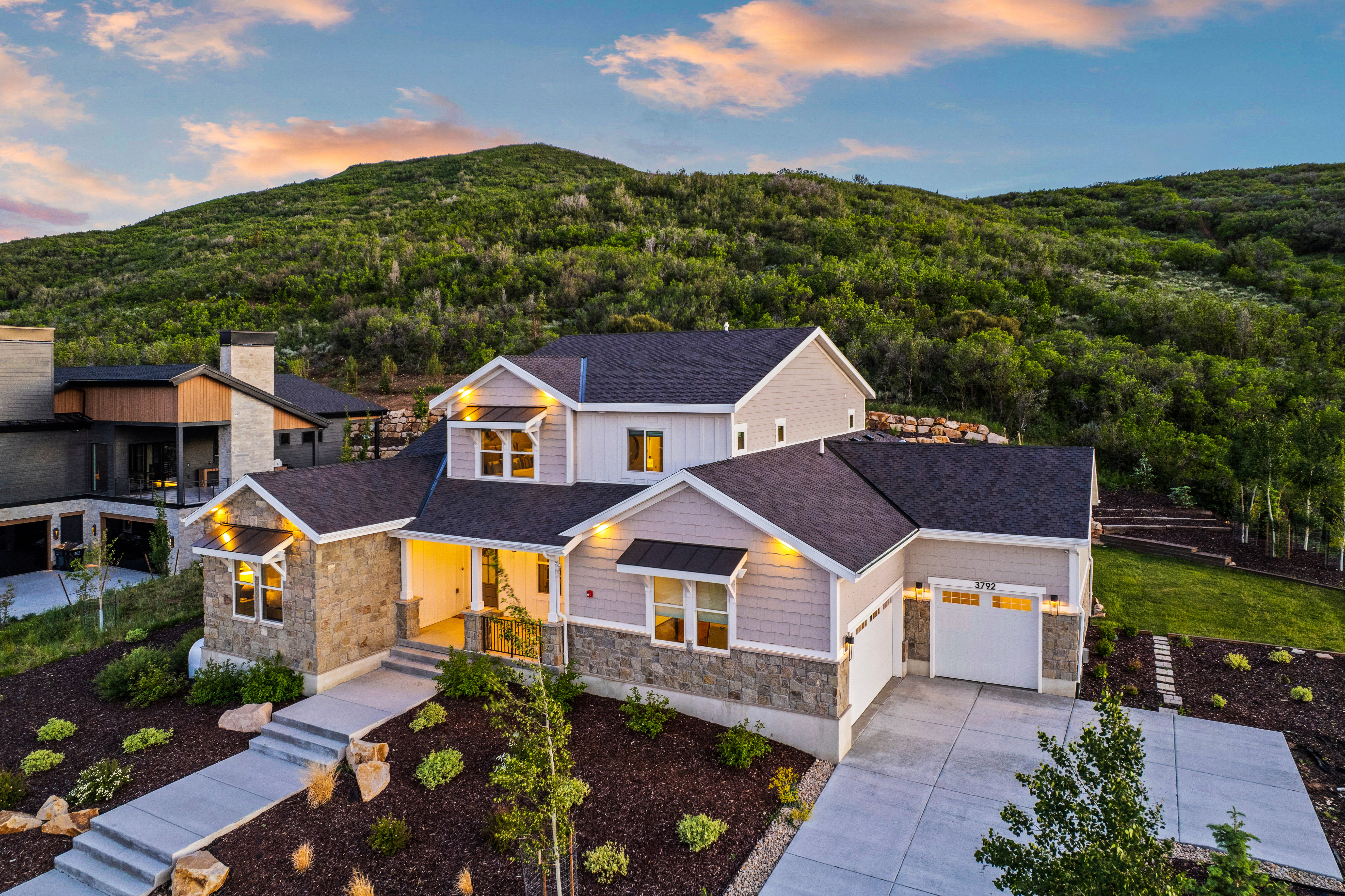 Contemporary residence featuring stone and siding exterior, a multi-car driveway, attached two-car garage, and tiered landscaping