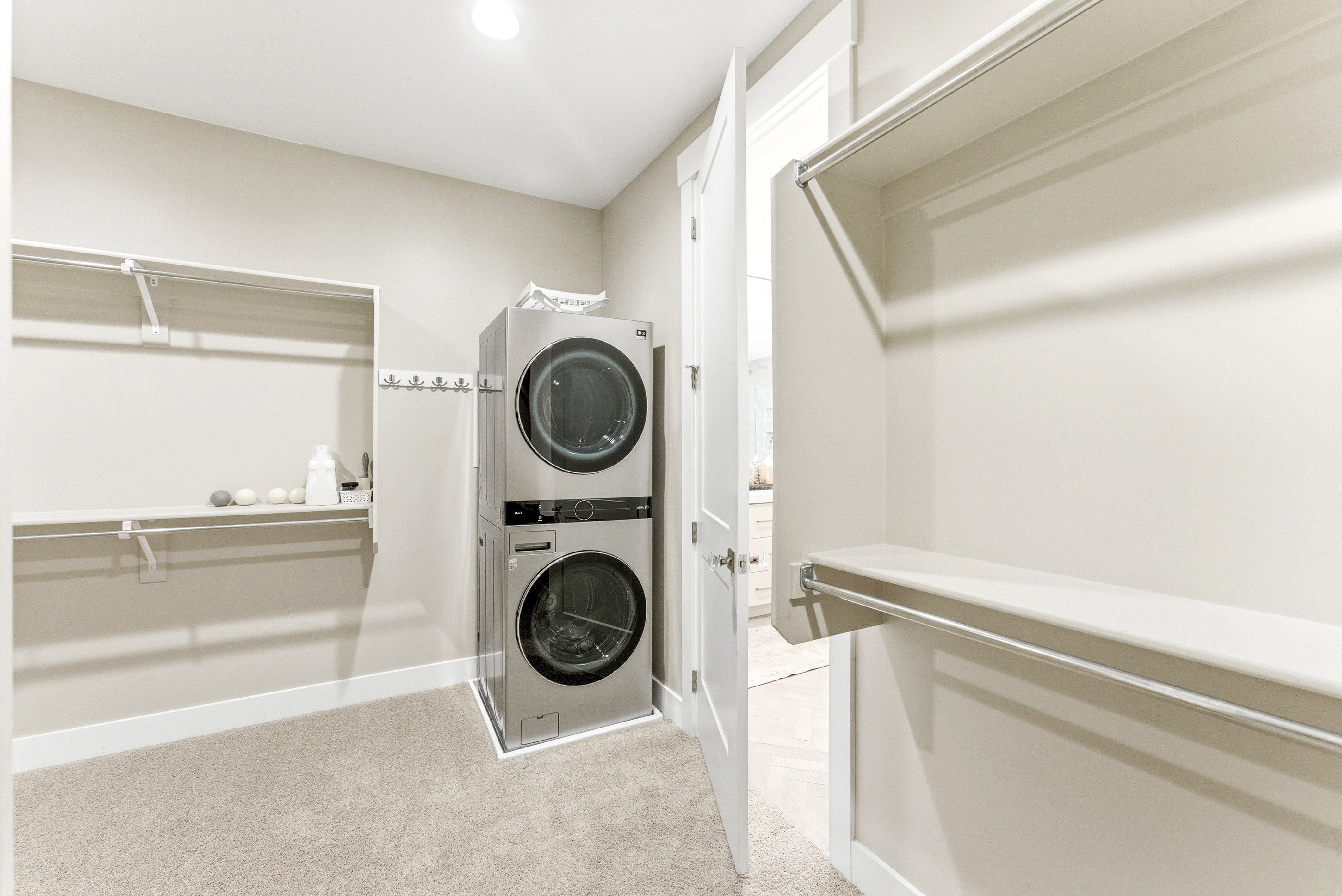 Dedicated laundry area featuring a stacked washer and dryer unit, integrated shelving, hanging rods, and light-toned carpeting