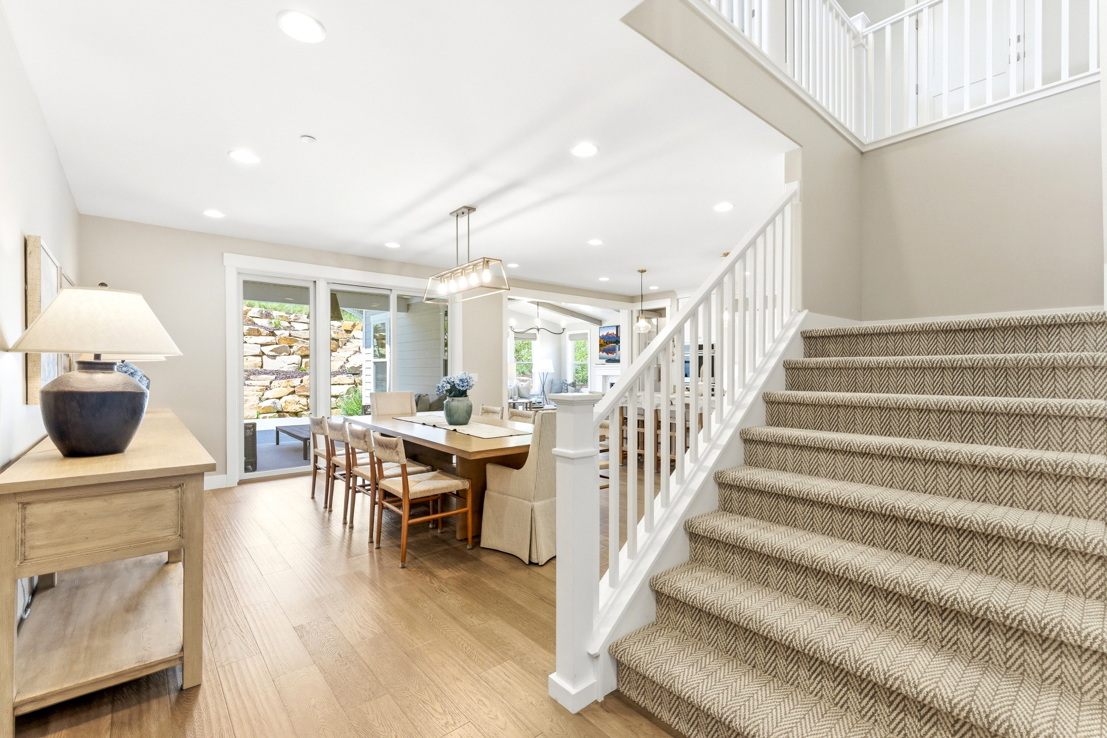 Two-story entryway featuring wood-finish flooring, a carpeted staircase with white balusters, recessed lighting, and a dining area with sliding glass doors