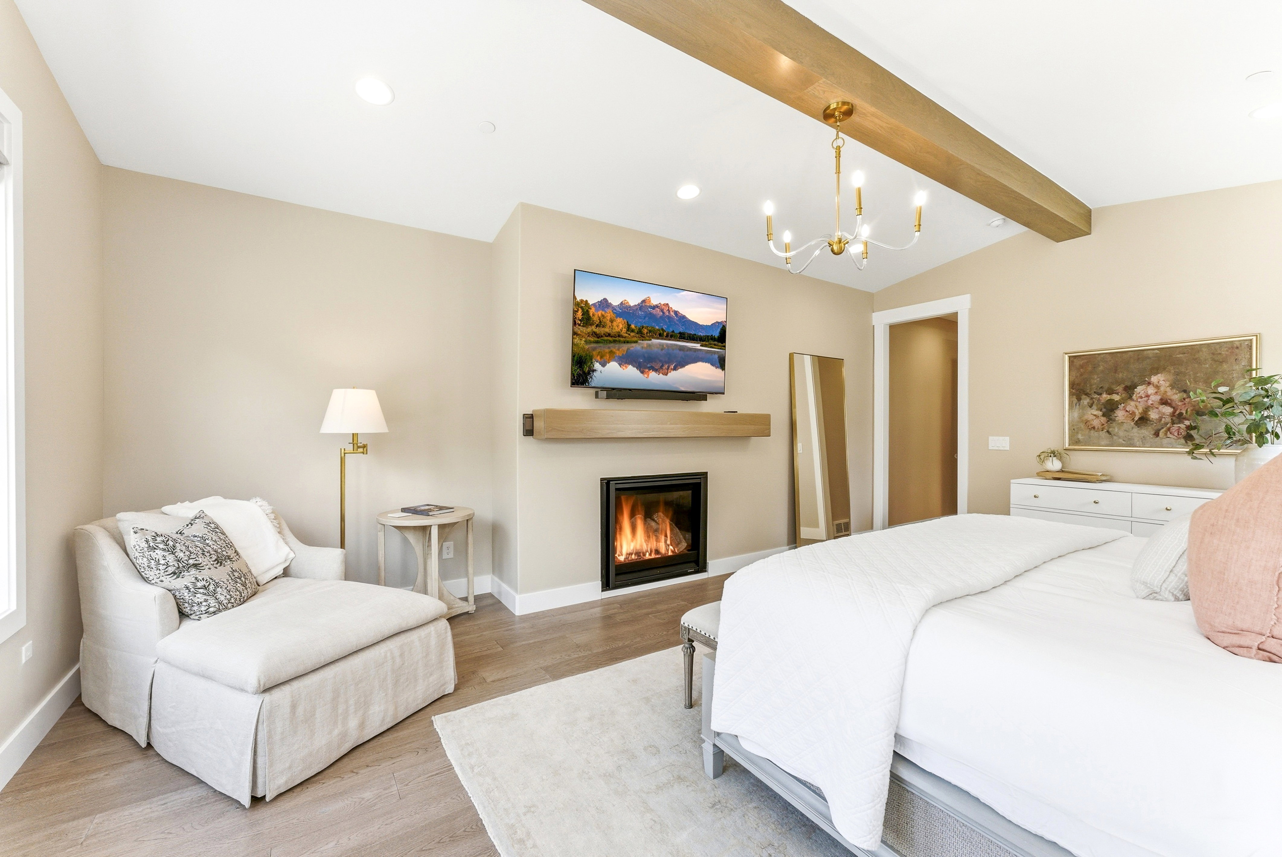 Spacious bedroom featuring vaulted ceilings with exposed wood beams, a built-in fireplace with a wood-finish mantel, and light wood-finish flooring