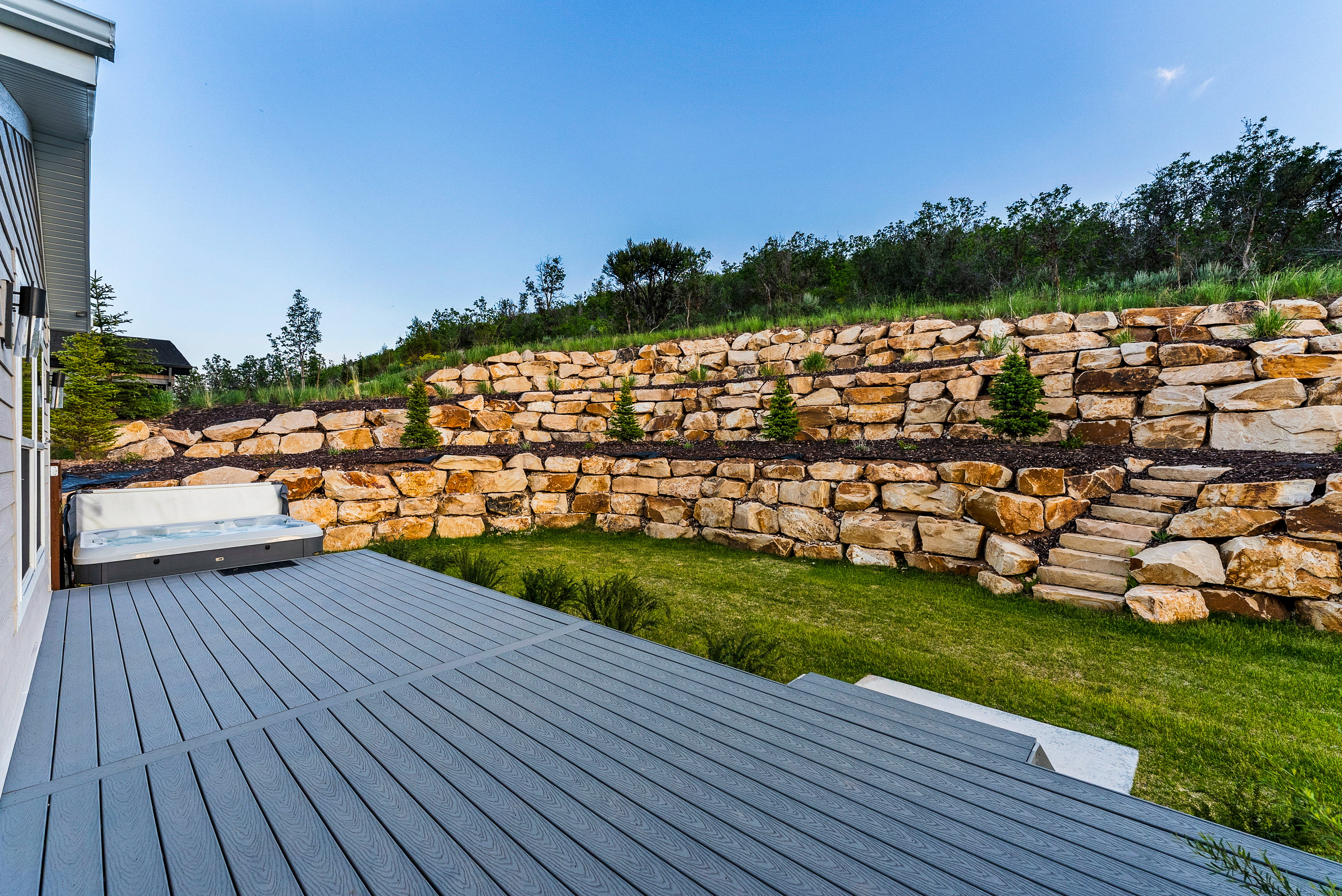 Expansive outdoor deck featuring composite decking, an integrated hot tub, and steps to a lawn area
