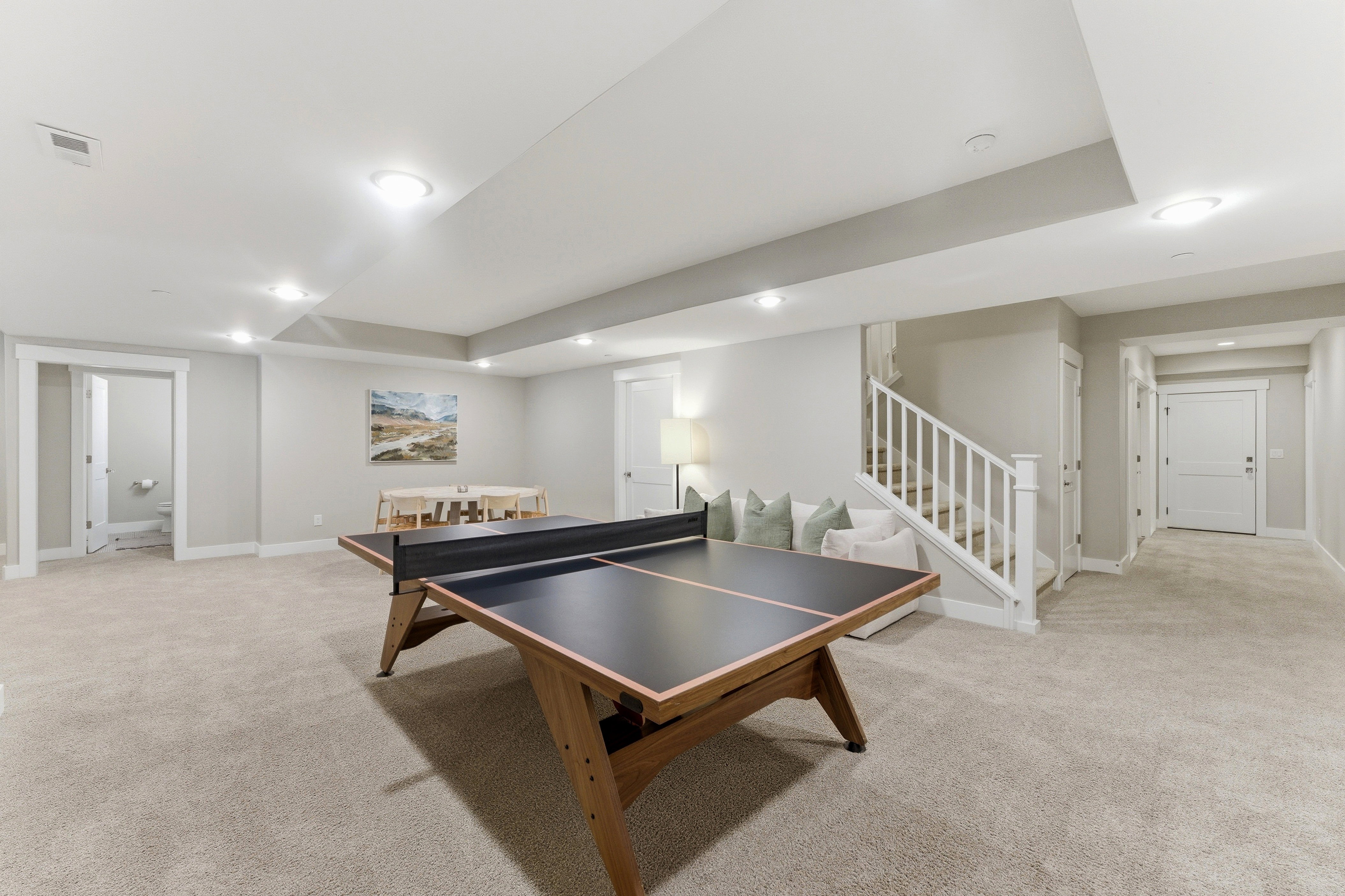 Expansive carpeted area featuring recessed lighting, a white painted staircase with wood handrail, and multiple doorways