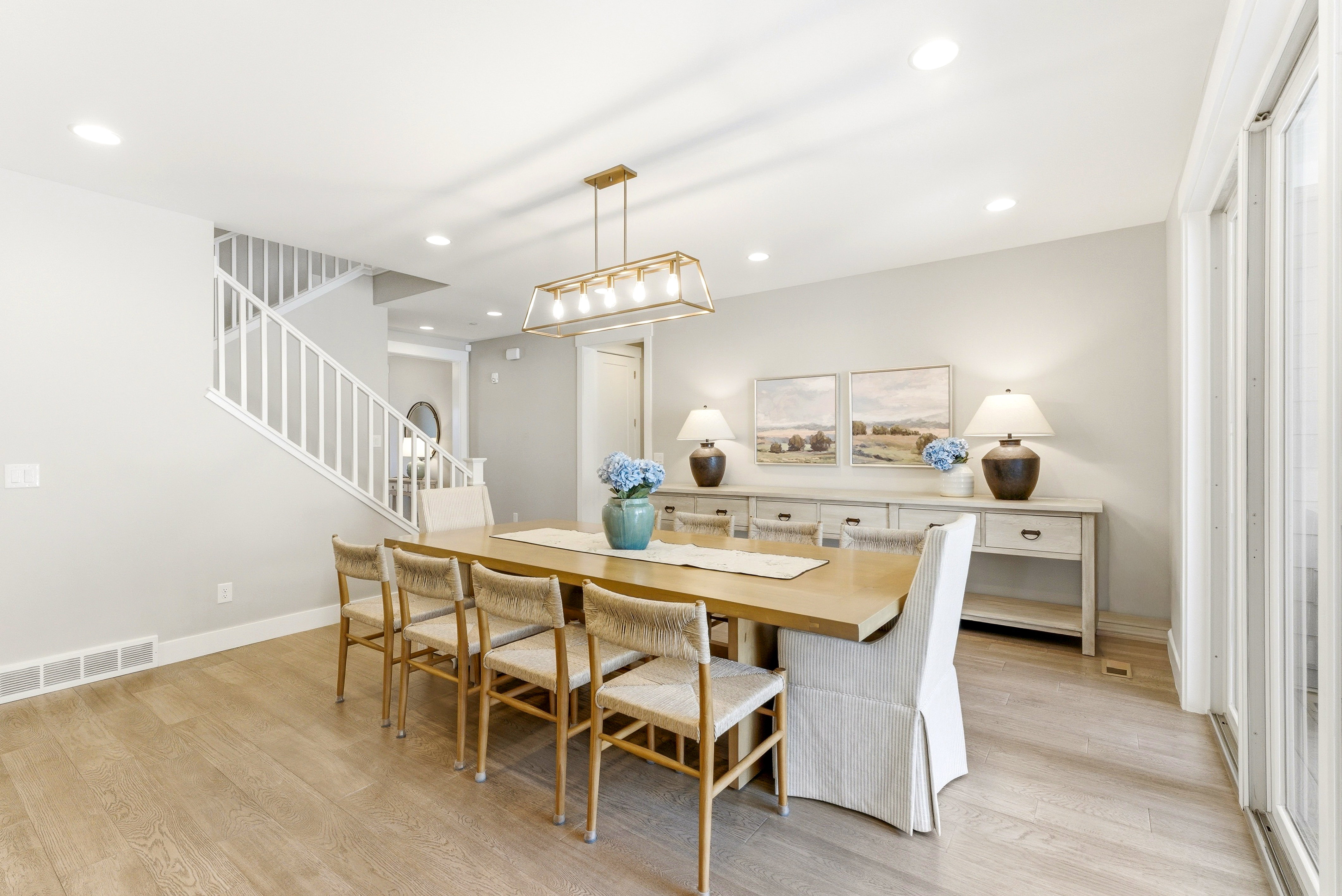 Spacious dining area featuring wood-finish flooring, a contemporary linear chandelier, recessed lighting, and a white staircase with open railings