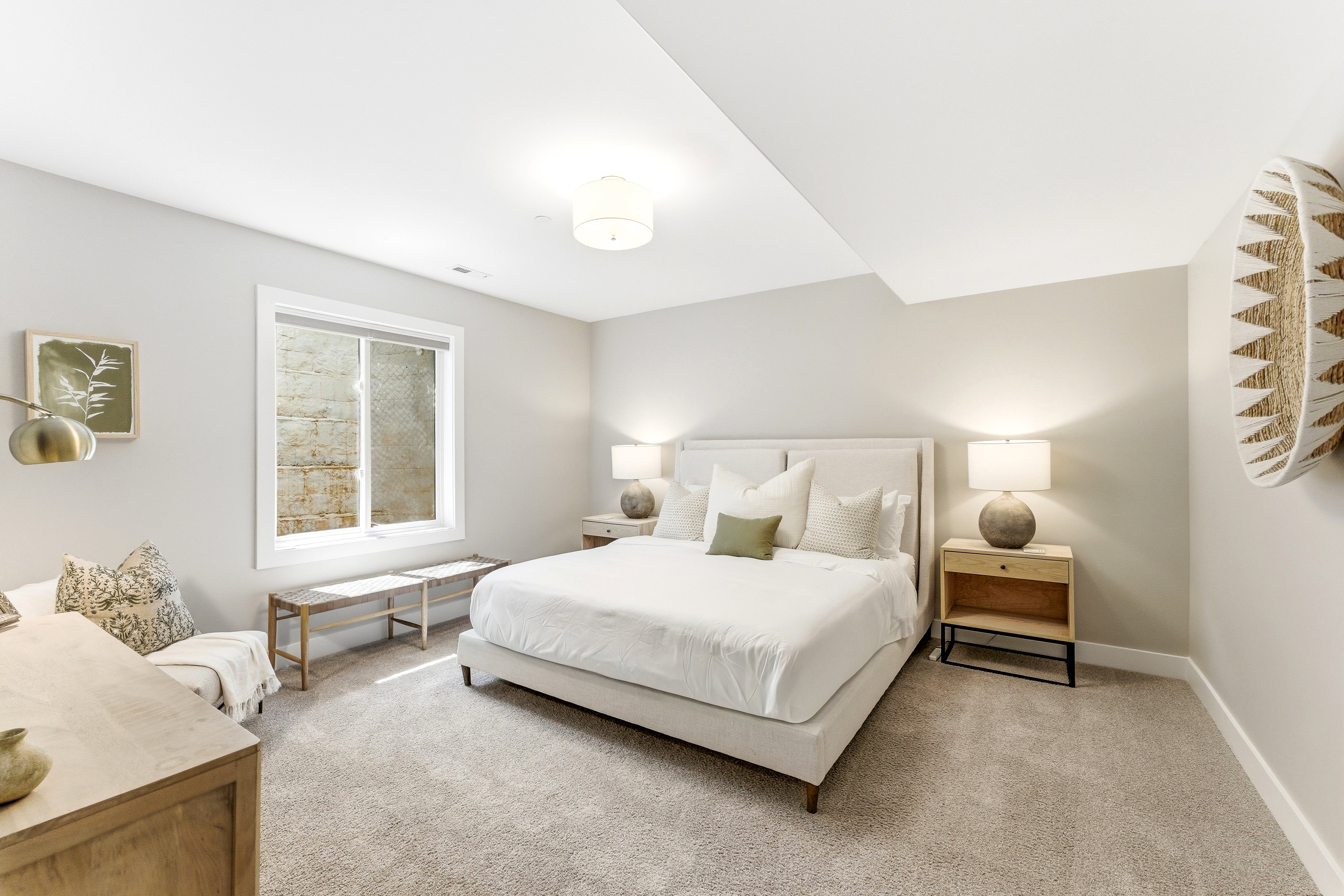 Carpeted bedroom featuring a light-colored upholstered bed frame with a padded headboard, a window with white trim, a built-in overhead light fixture, and light gray wall paint