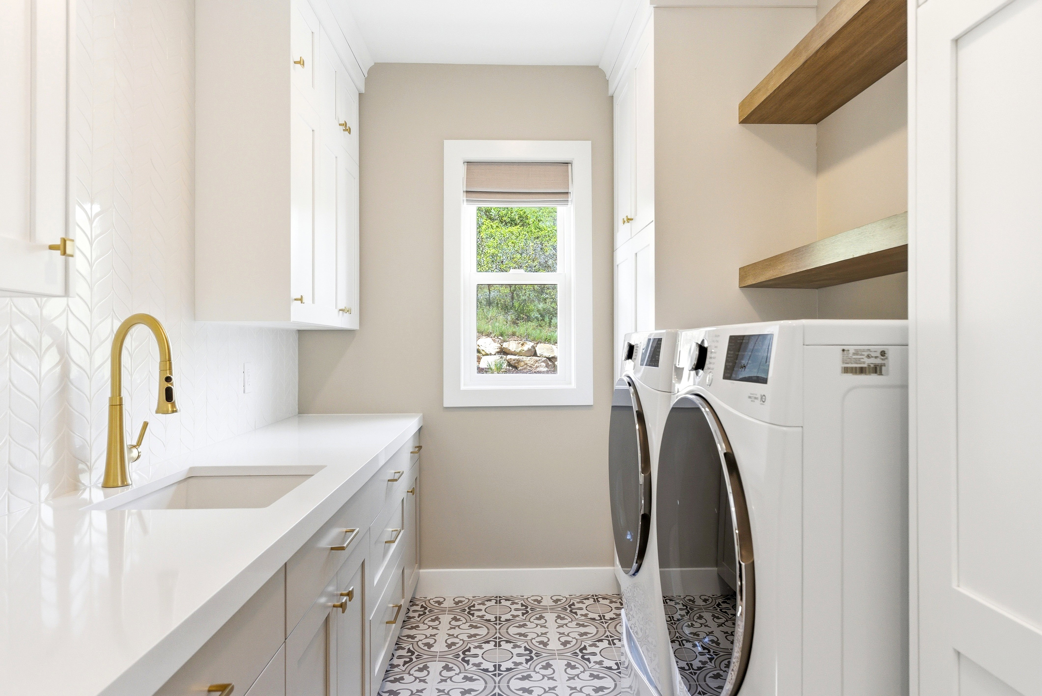 Functional utility room featuring a large undermount sink with a brass-finish faucet, extensive countertop space, and patterned floor tile