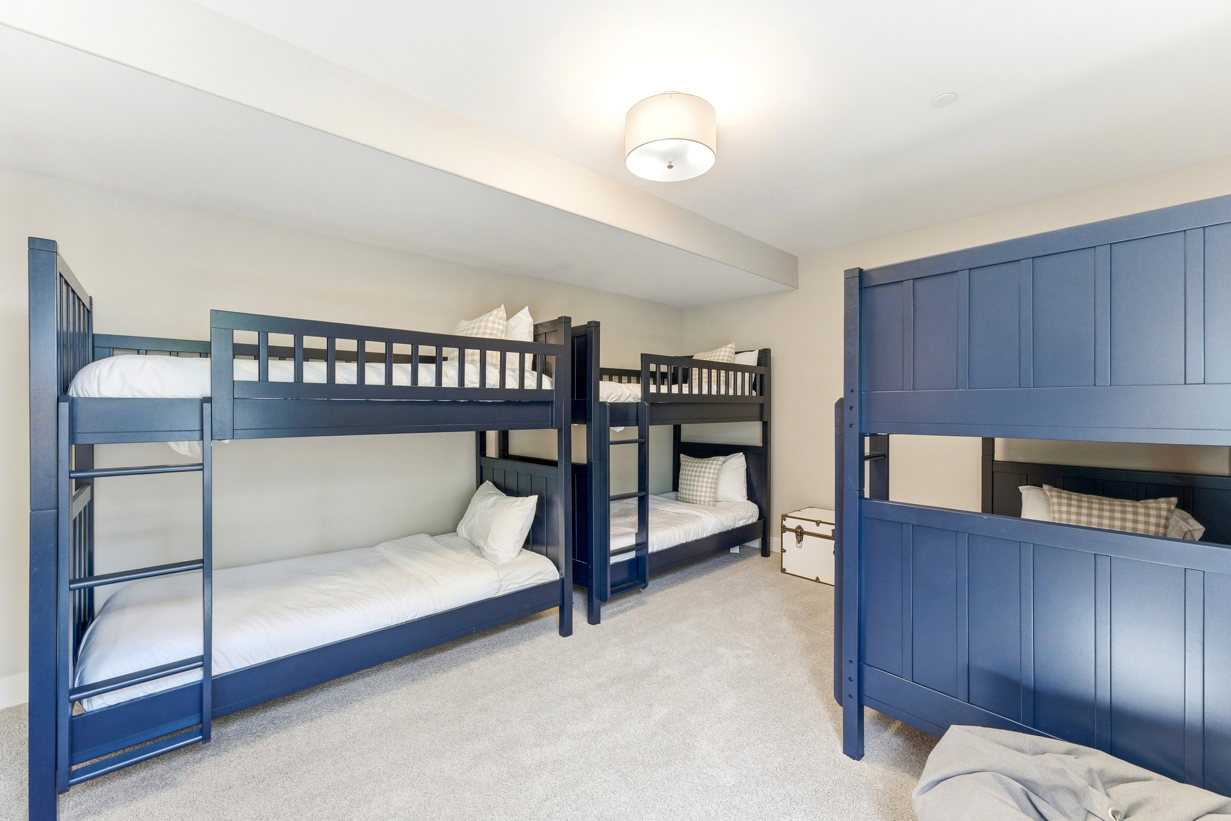 Spacious room featuring light gray carpeting, neutral wall tones, and multiple blue-painted bunk beds