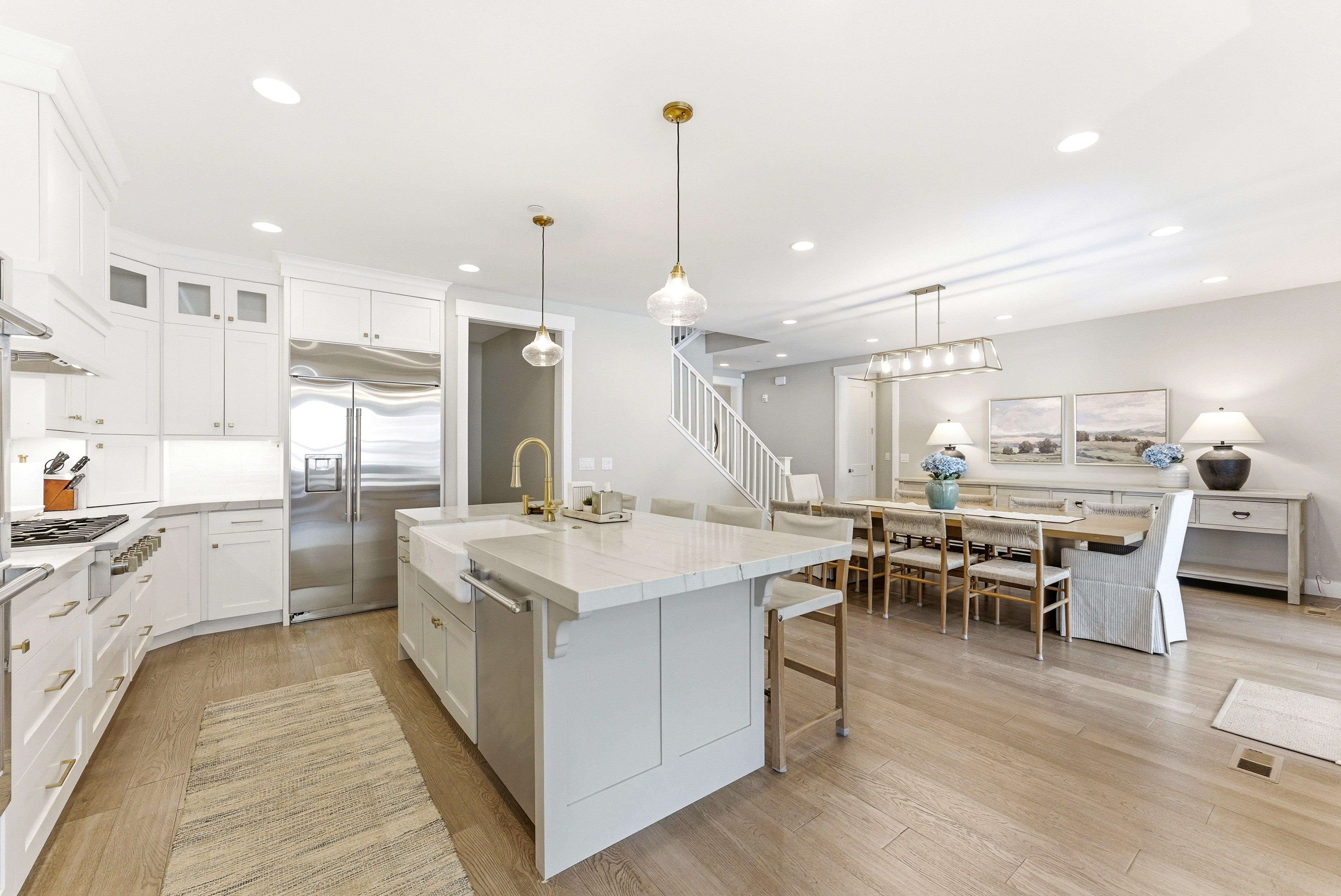 Open-concept kitchen and dining area featuring light wood-finish flooring, white cabinetry, a large kitchen island with countertop seating, stainless steel appliances, and recessed lighting throughout
