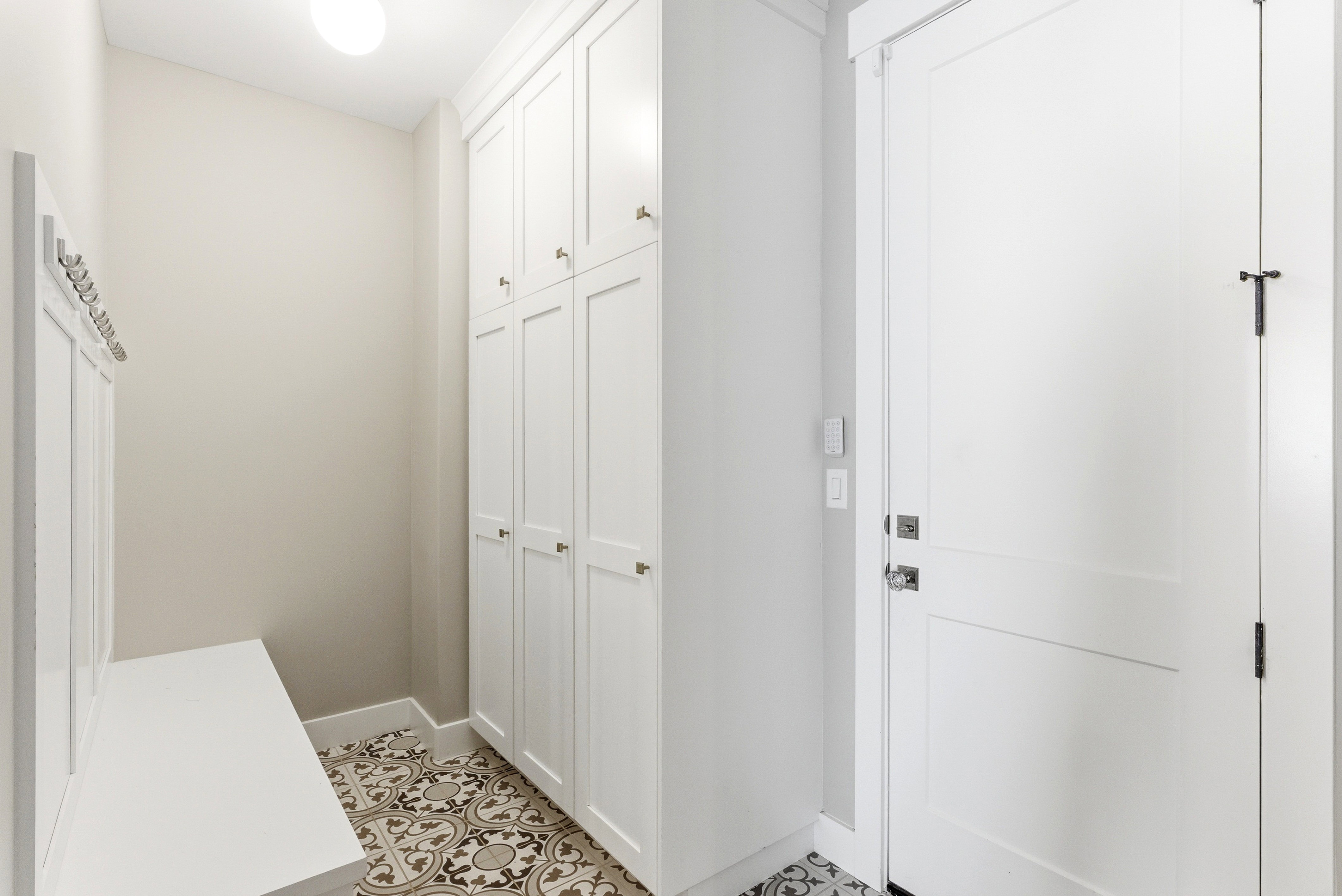 Entryway featuring patterned tile flooring, built-in storage cabinetry with gold-tone hardware, and a white built-in bench with coat hooks