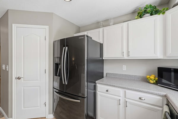 Kitchen area featuring white cabinetry with silver hardware, speckled gray countertops, and a modern dark stainless steel refrigerator