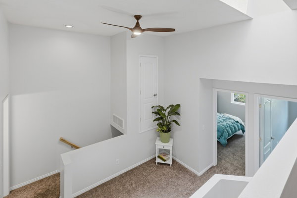 Upper-level landing featuring textured carpeting, a white painted railing with a natural wood handrail, and a contemporary ceiling fan