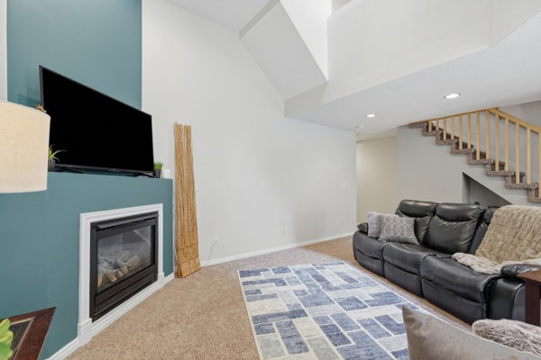 Living area featuring a corner fireplace with white trim, a high ceiling, recessed lighting, and a carpeted staircase with wood banister